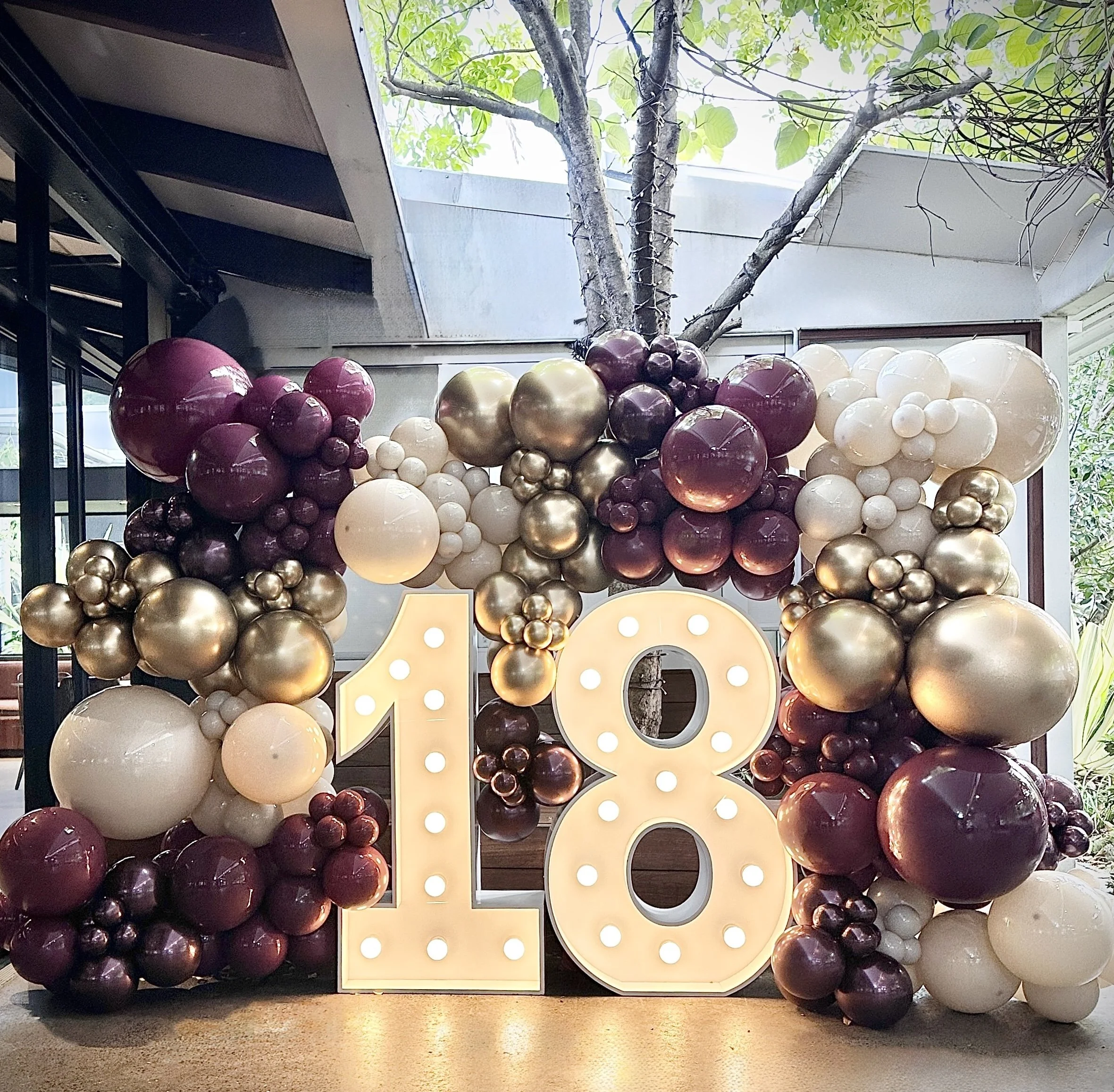 Deep plum tones paired with pops of jewel hues for an eighteenth birthday party. Balloon wall around a light up number 18