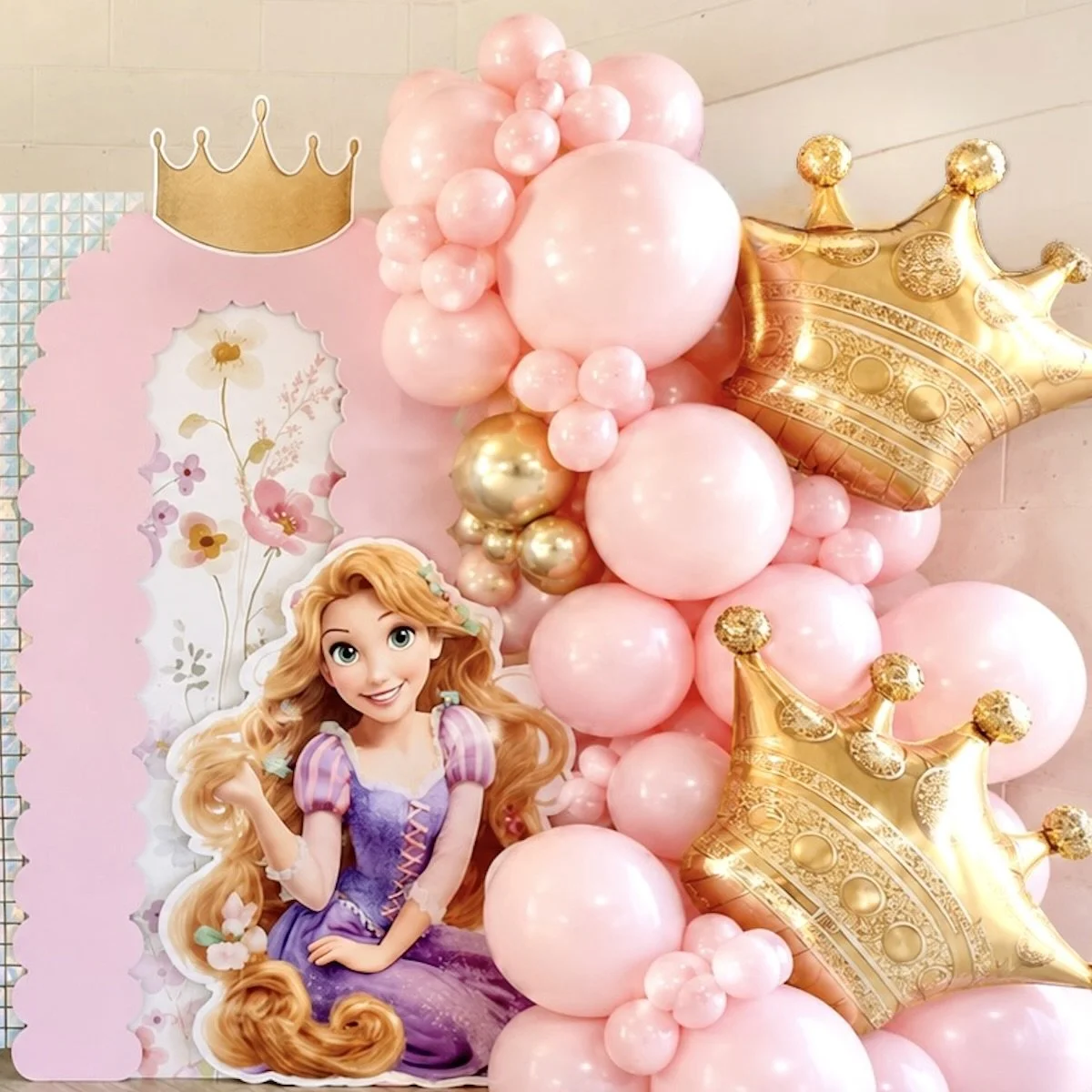 Decorative birthday display with a Rapunzel theme, featuring pink and gold balloons, a large Rapunzel cutout, and a gold crown-shaped balloon.