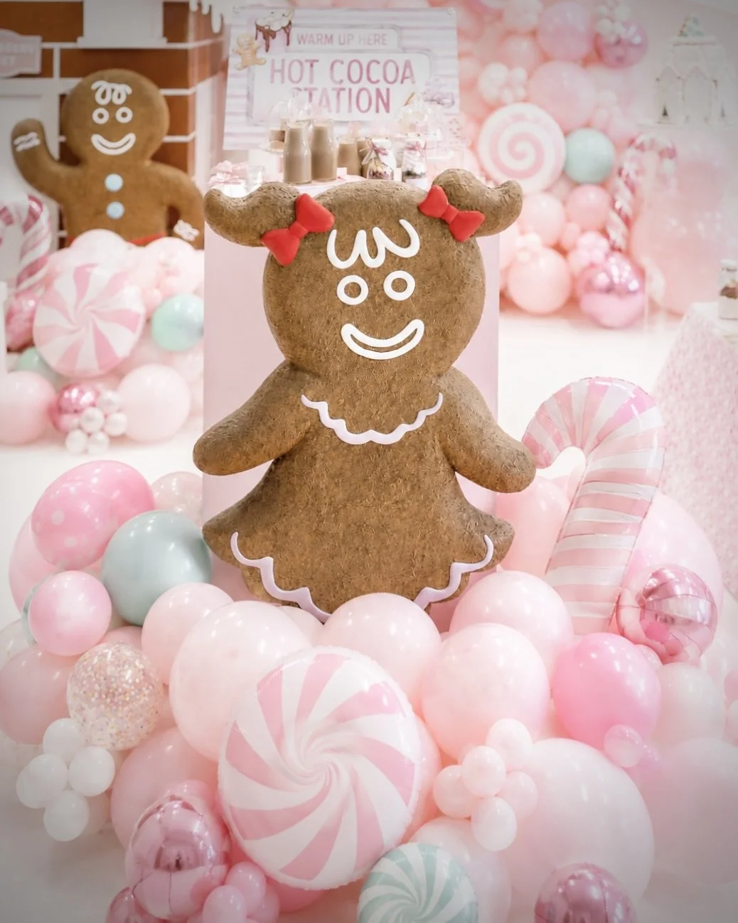 Gingerbread girl cookie with red bows, white facial decorations, and pink balloons at a pink-themed party setup.