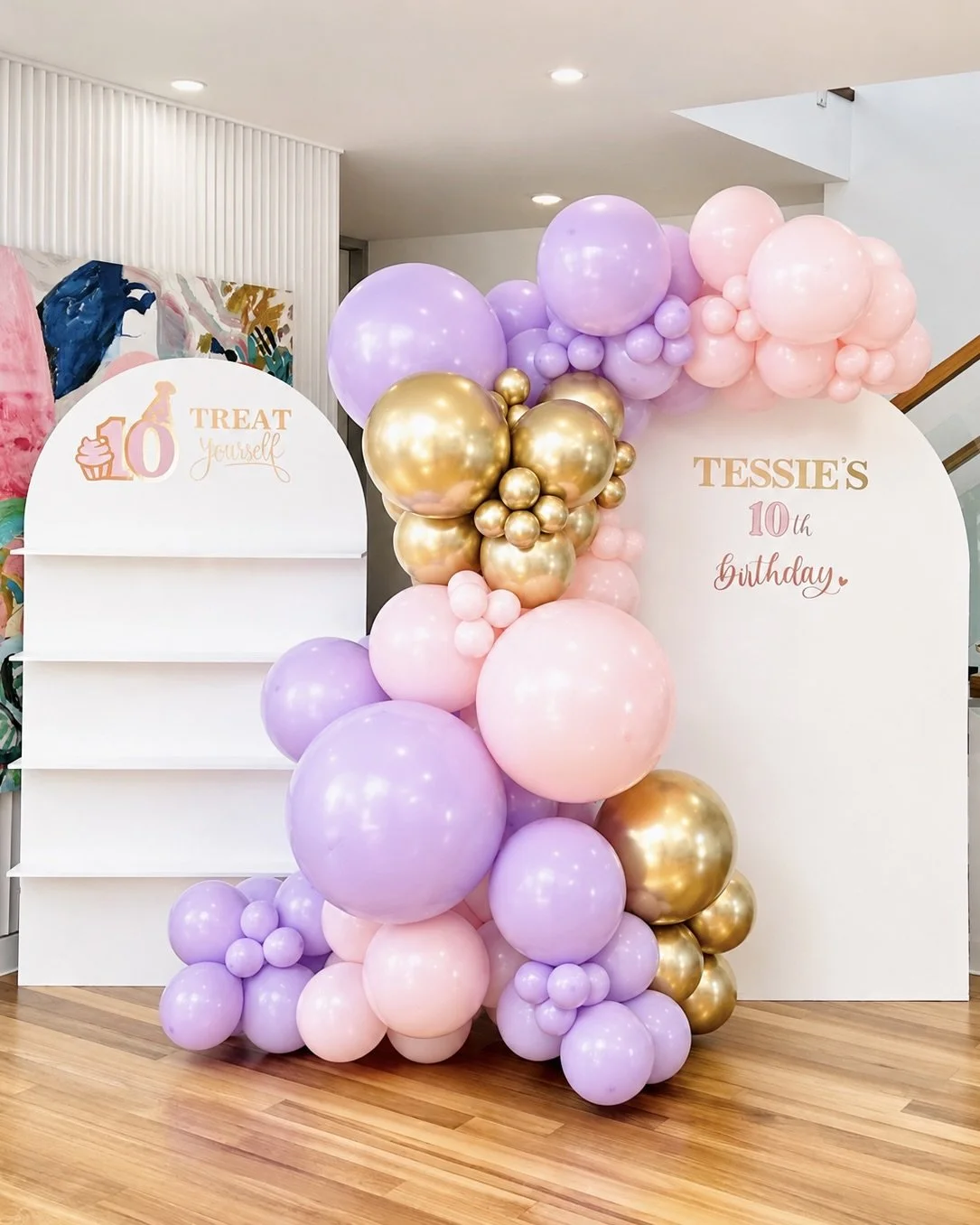 Decorative birthday display with pastel pink, purple, and gold balloons, and a white backdrop with birthday messages for Tessie's 10th birthday.