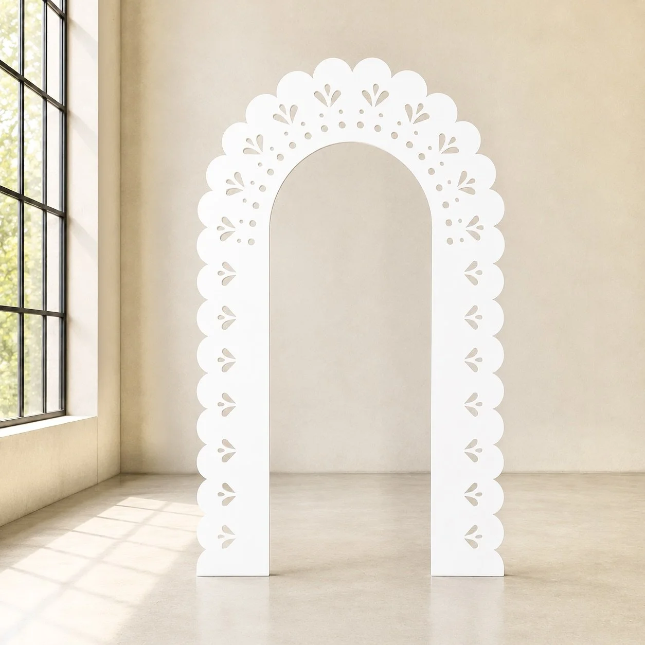A white decorative arch with floral cutout patterns stands in a bright, minimalistic room with large windows and beige walls.