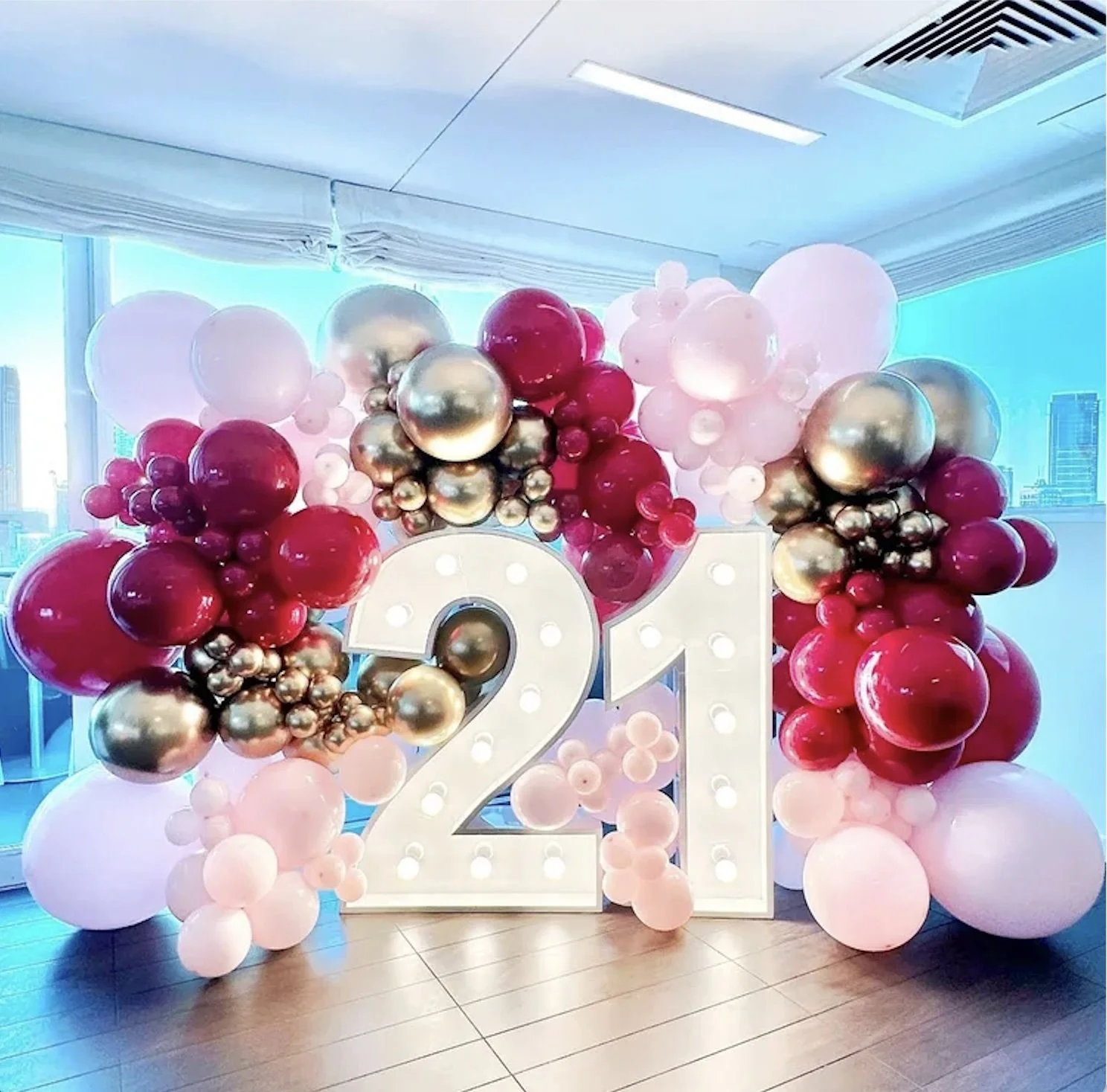 Jewel toned balloon arch surrounds a large illuminated number 21, celebrating a 21st birthday