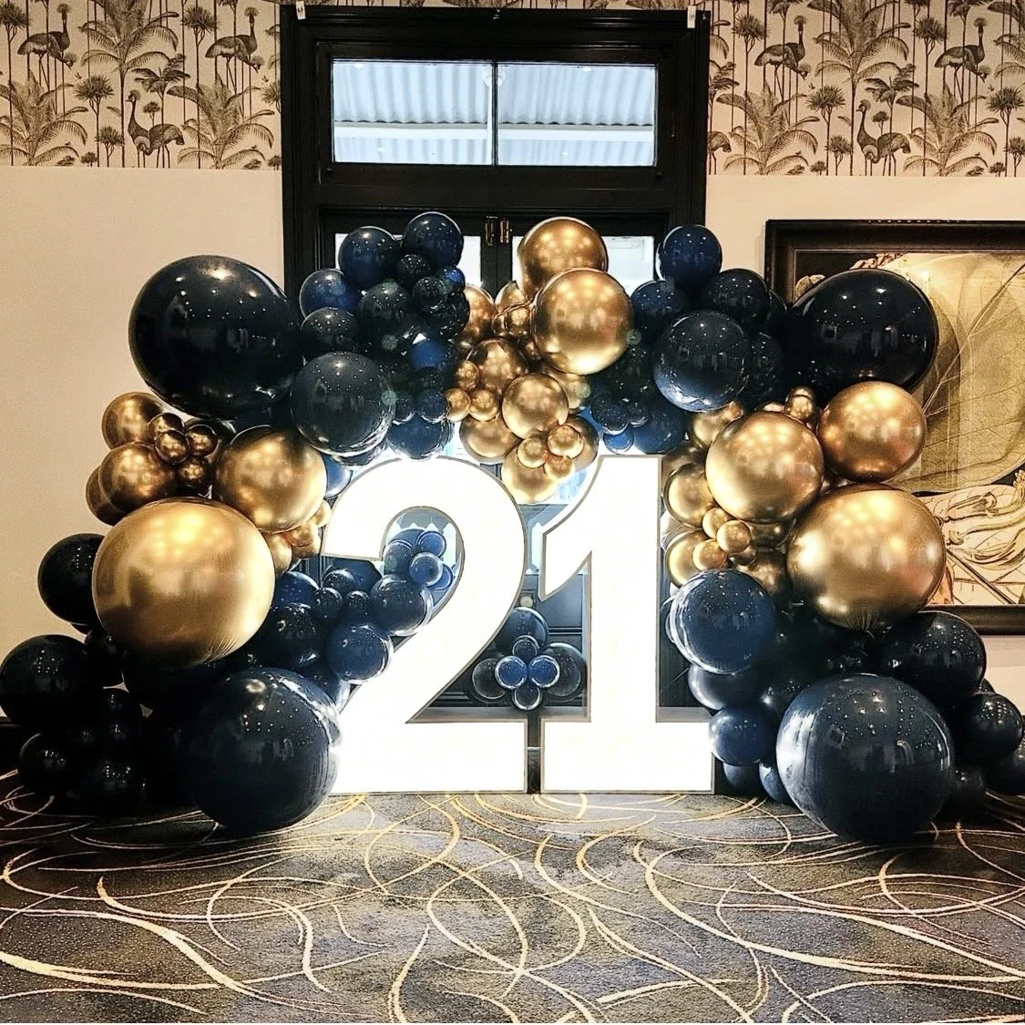 Large illuminated number 21 surrounded by black and gold balloon wall