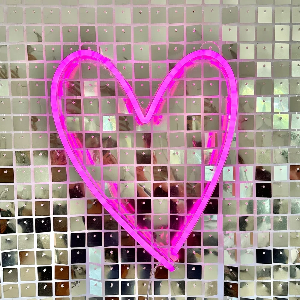 Pink neon heart on a silver shimmer wall
