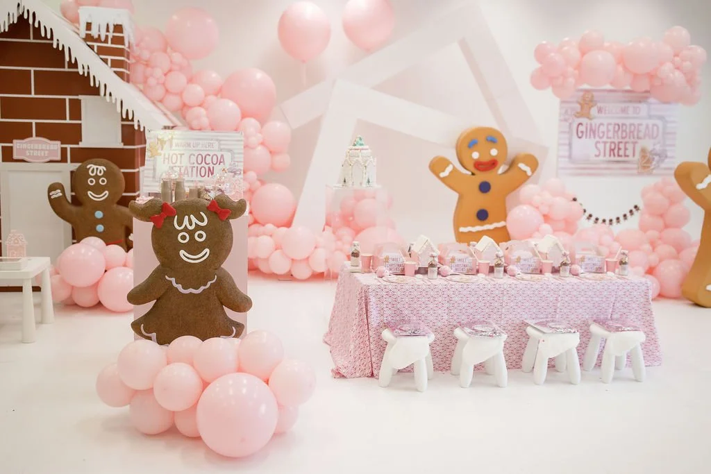 Gingerbread-themed birthday party setup with pink balloons, gingerbread cookie decorations, and a pink table with milk cartons and small chairs
