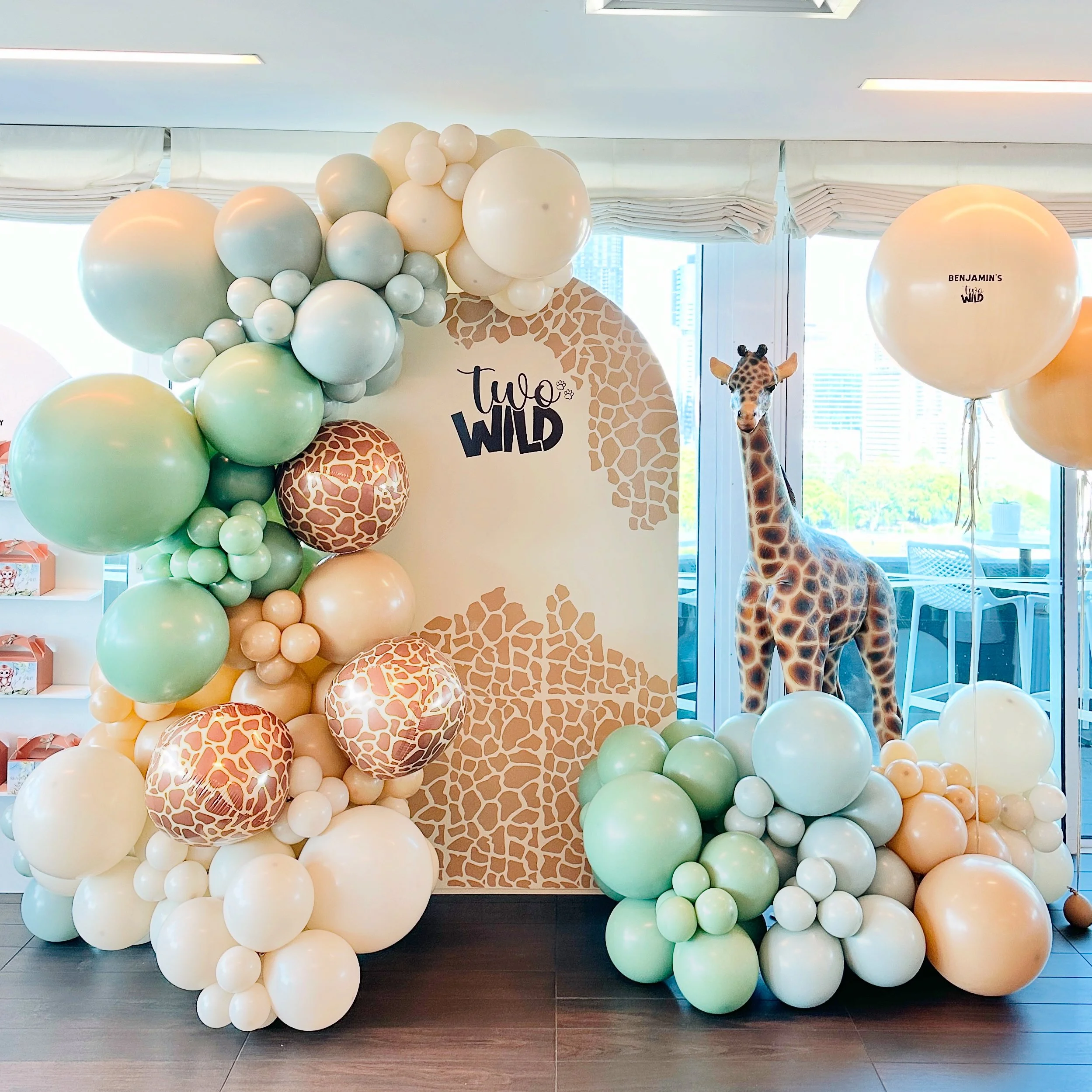 A jungle-themed backdrop with balloons and a giraffe plush toy at a zoo or safari-themed event.