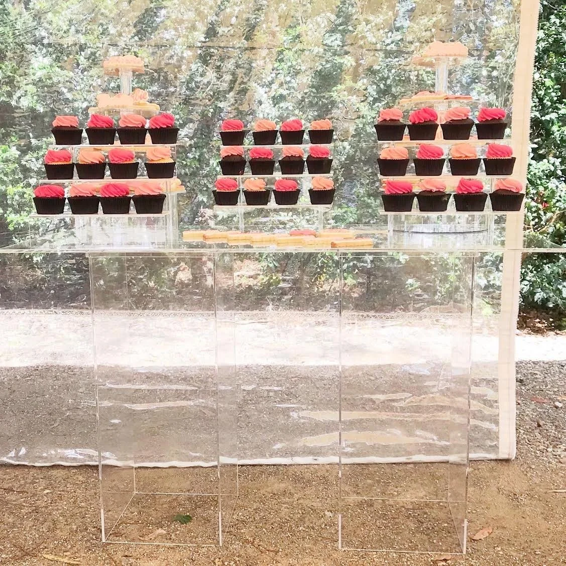 Clear acrylic dessert table displaying cupcakes and cookies on transparent dessert risers