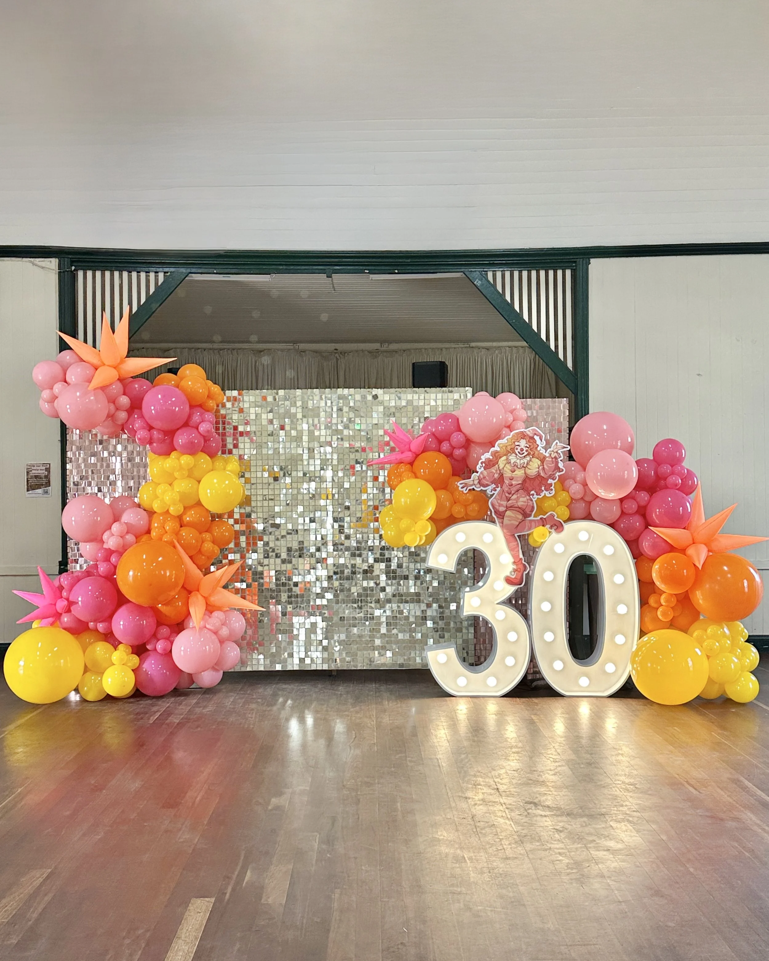 Vintage clown themed 30th birthday featuring a gold shimmer wall, balloons and a light up number 30 with a retro clown cut out