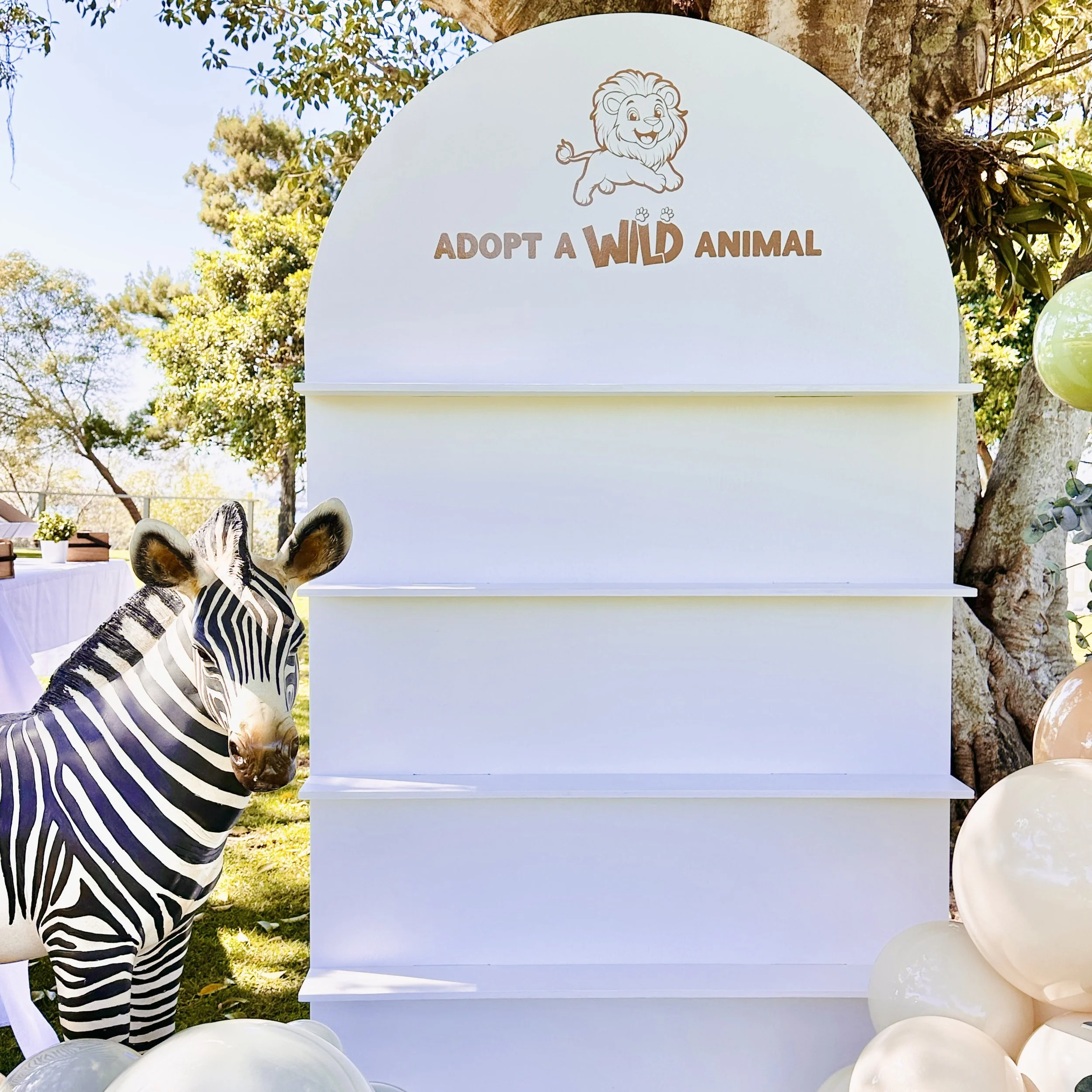 Wild One 1st Birthday party. A treat wall backdrop showcasing party favours with the phrase 'Adopt a Wild Animal'