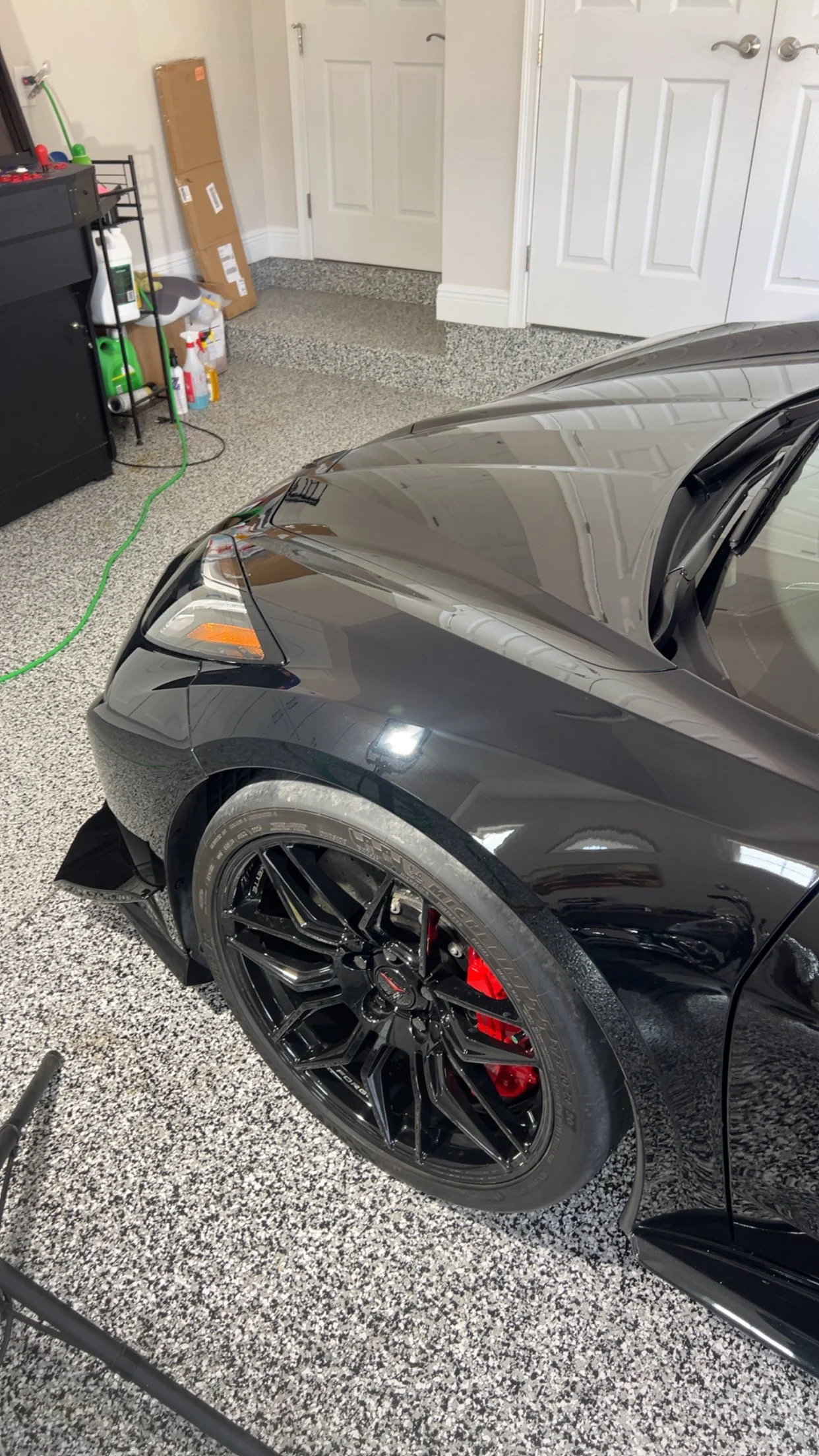 Close-up of the front part of a black sports car with red brake calipers parked in a garage.