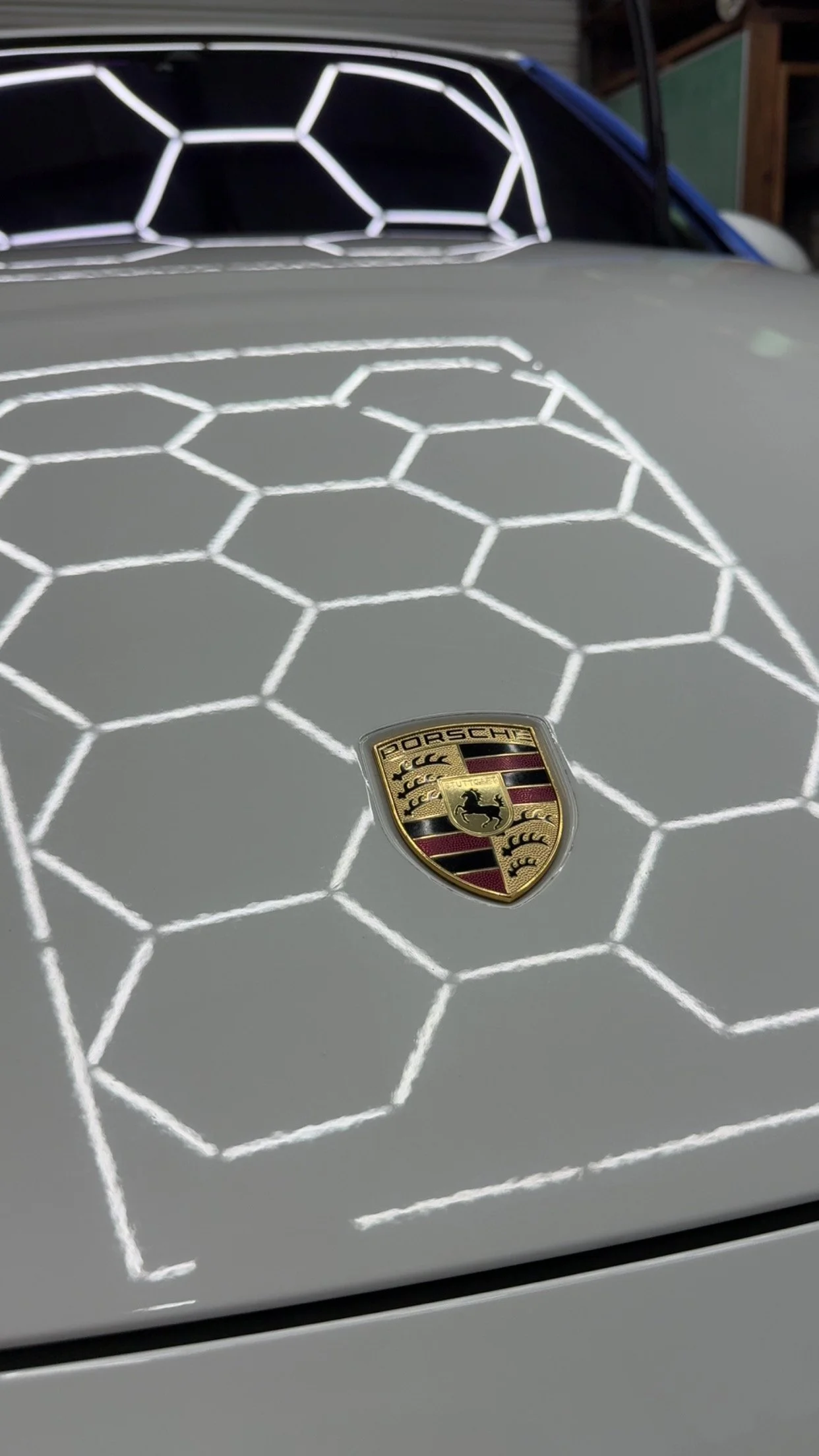 A close-up of a Porsche car hood with a white hexagon pattern and the Porsche emblem in the center.