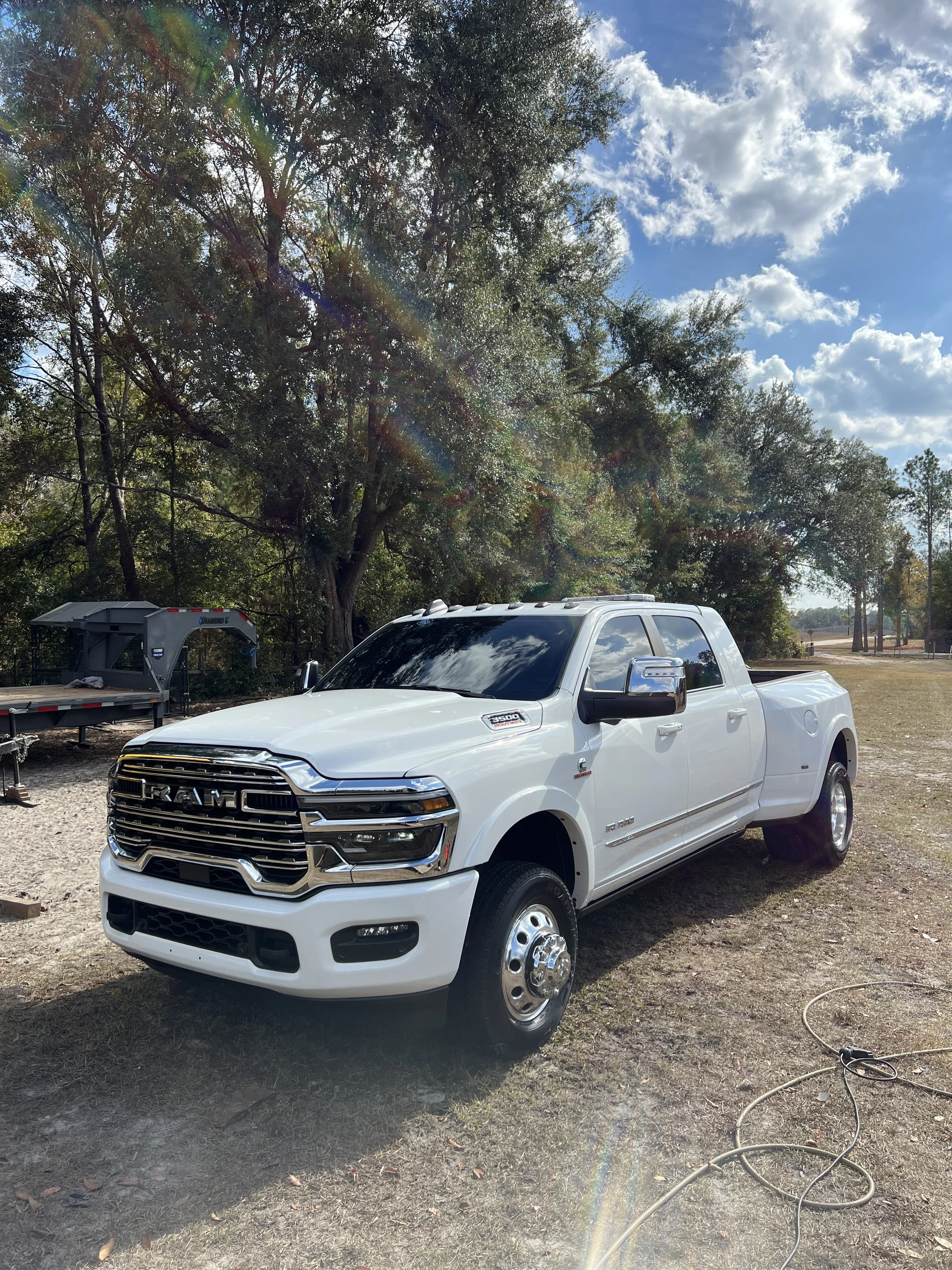 A white RAM pickup truck parked outdoors on grassy ground with trees and a partly cloudy sky in the background.