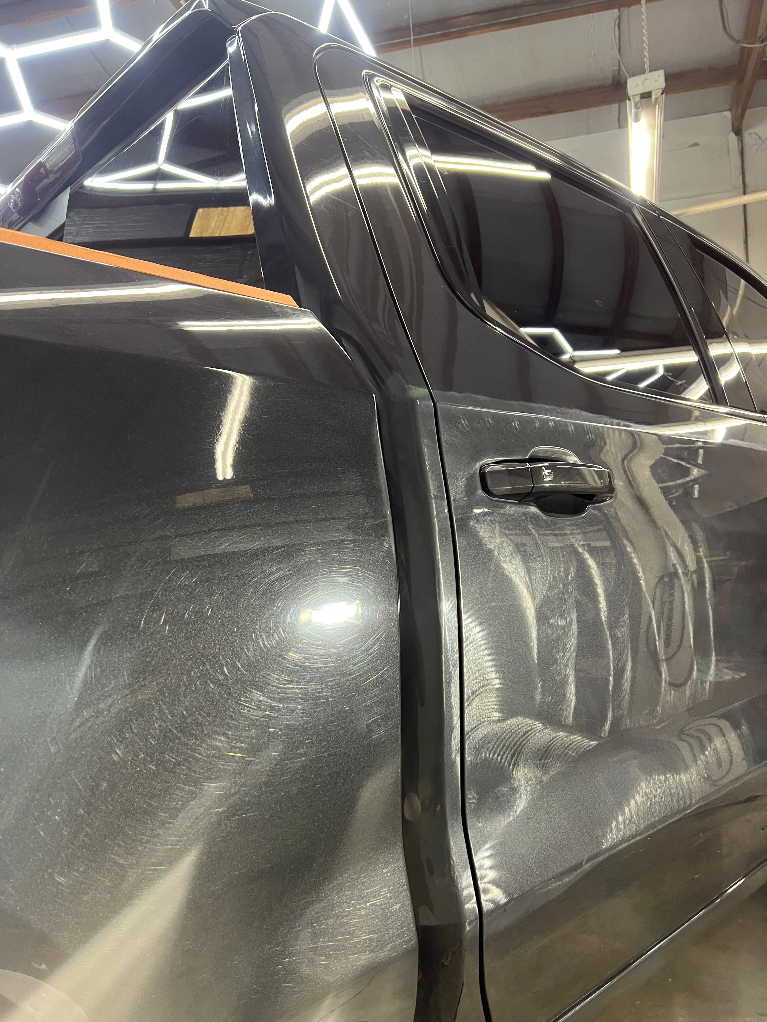 Close-up of a black car with visible scratches on the door, inside a garage with bright overhead lighting.