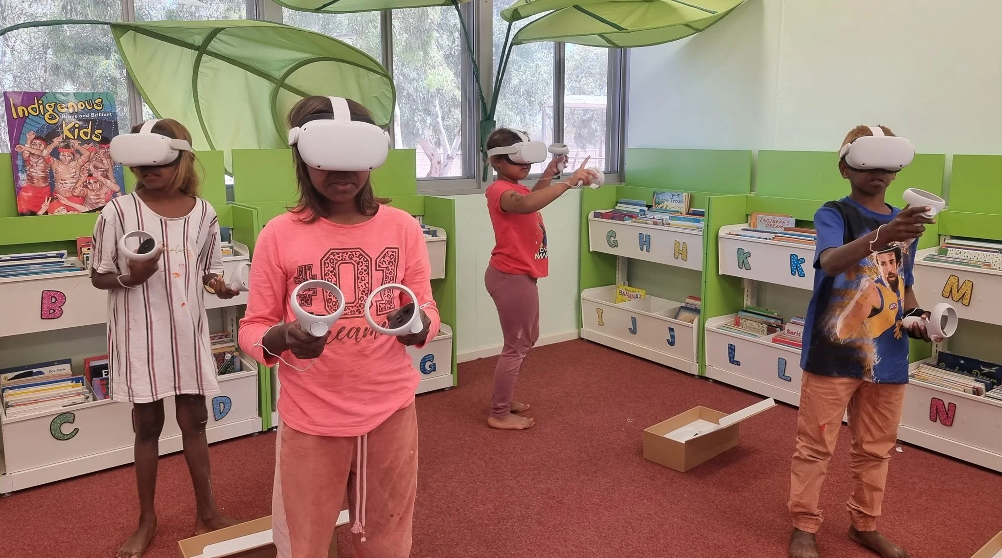 Four children in Wiluna Community School library wearing virtual reality headsets holding VR controllers.
