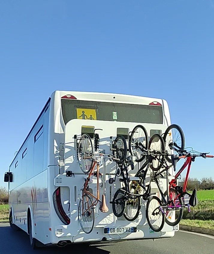 Un bus blanc avec porte-vélos et plusieurs vélos attachés à l'arrière.