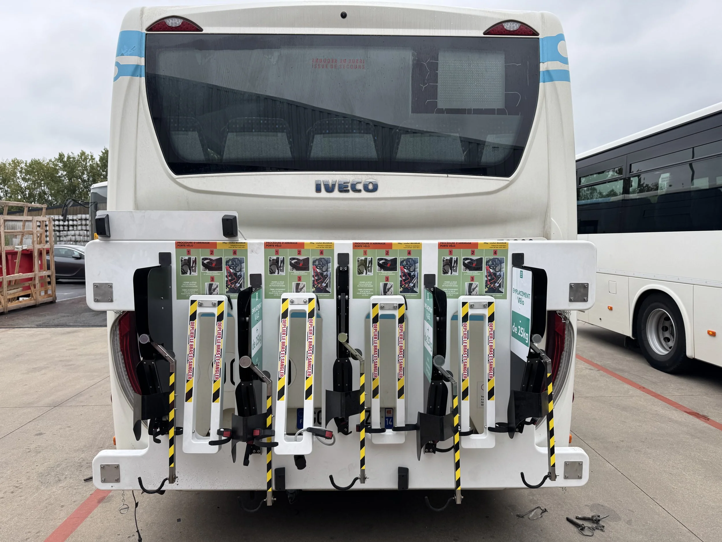 Un bus blanc avec un porte-vélos à l'arrière chargé de plusieurs vélos électriques. Le bus est stationné dans un parking, avec d'autres bus visibles à côté.
