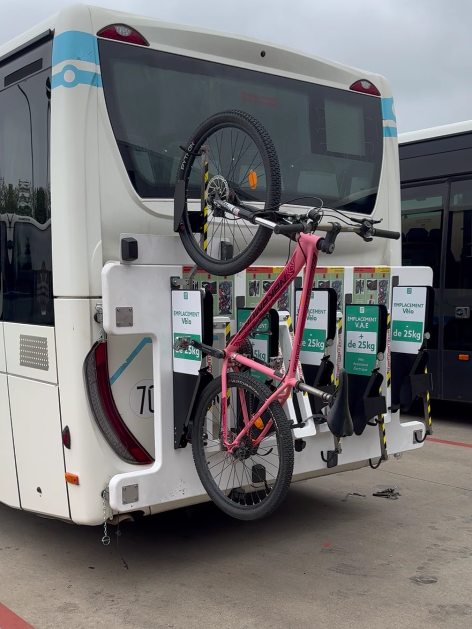 Un bus avec un porte-vélos contenant deux vélos, dont un vélo rose attaché dans un parking.