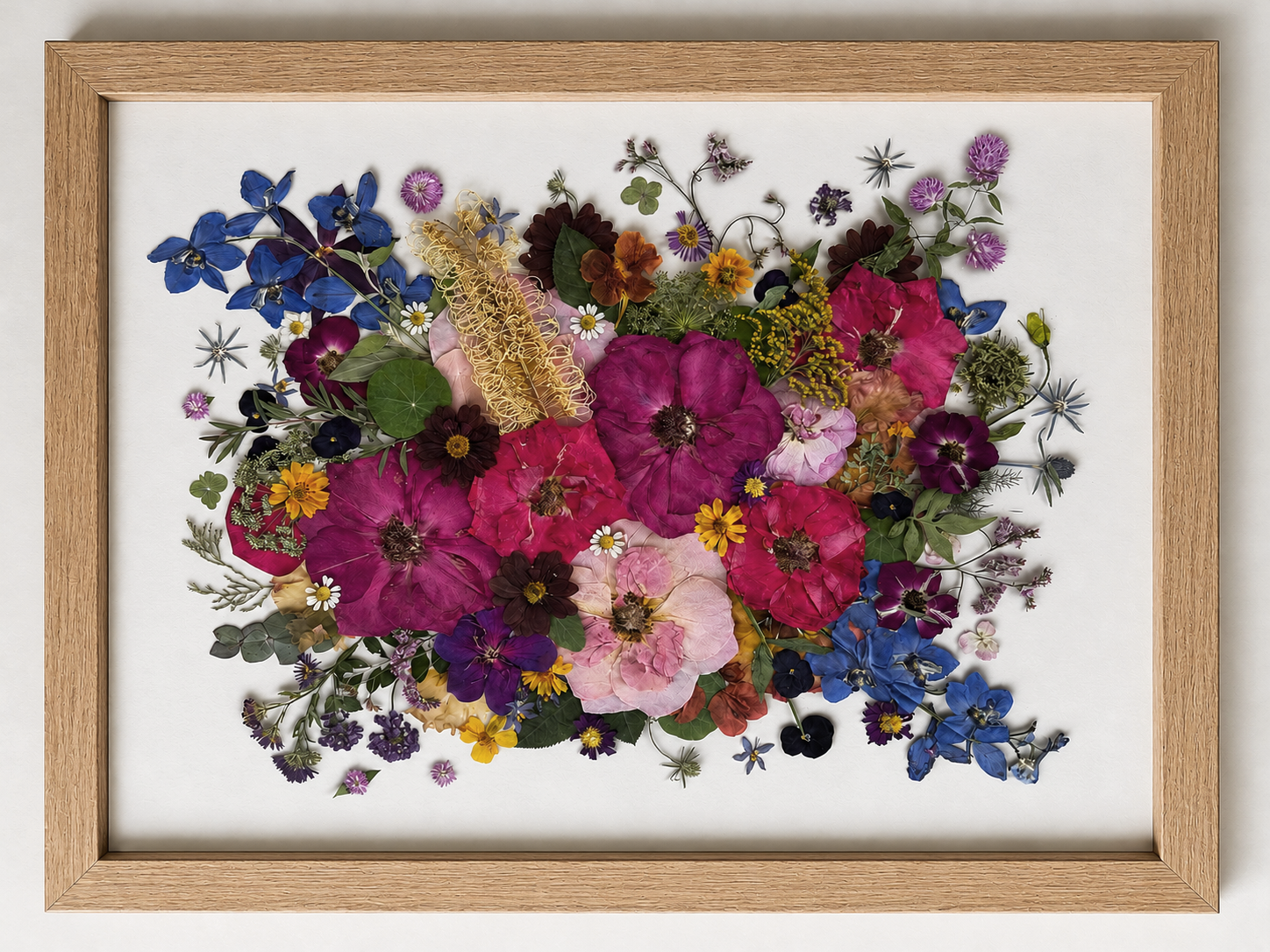 A framed floral arrangement of dried and pressed flowers with various colors and types, displayed on a white background.
