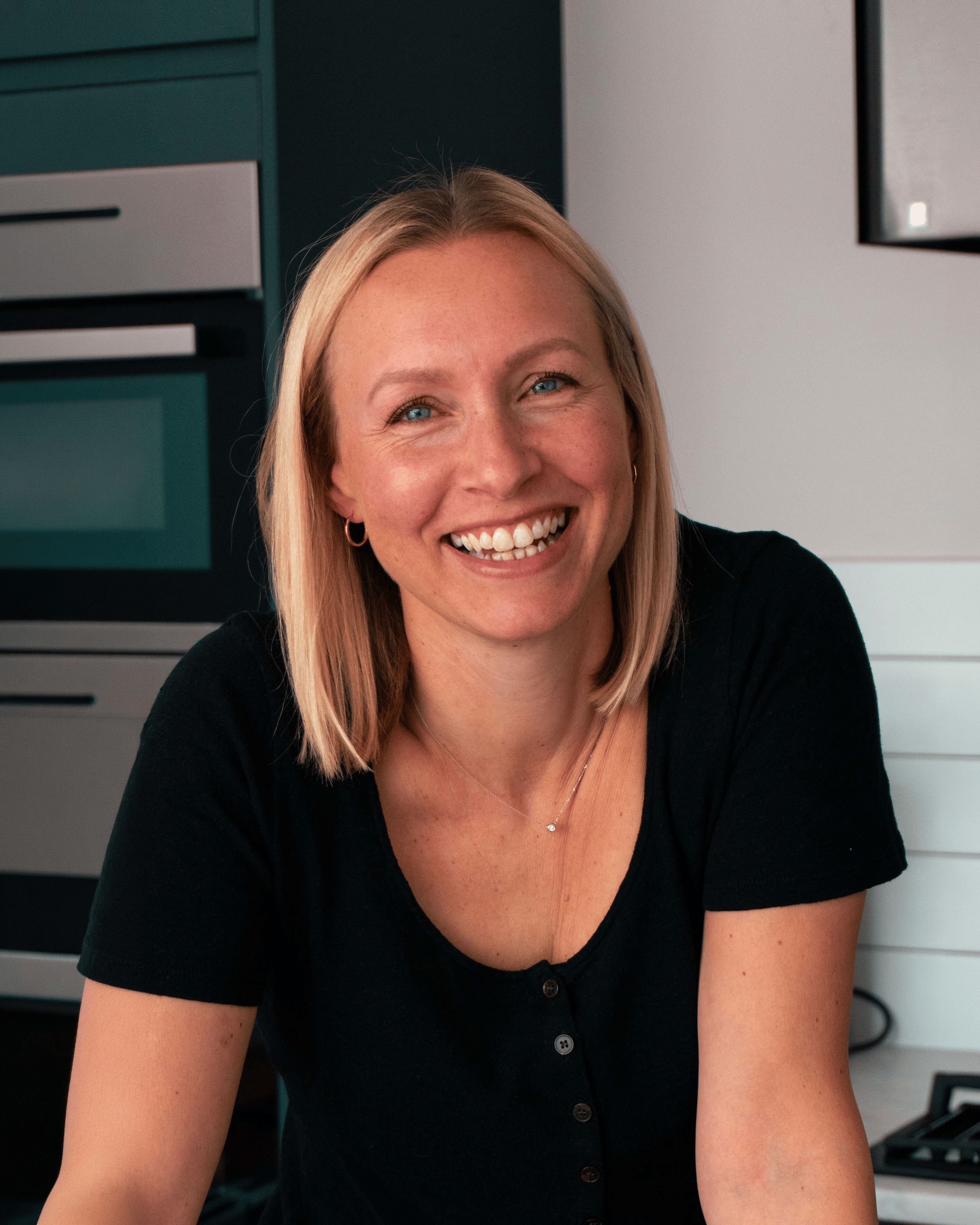 Rowan smiling, wearing a black top, in a kitchen setting.