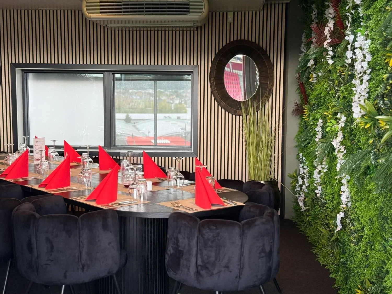 Innendørsrestaurantdekning med svart bord og krøllete svarte stoler, dekket med røde servietter og opp-ned glass.