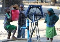 Niños jugando alrededor de una rueda de agua en un espacio al aire libre.