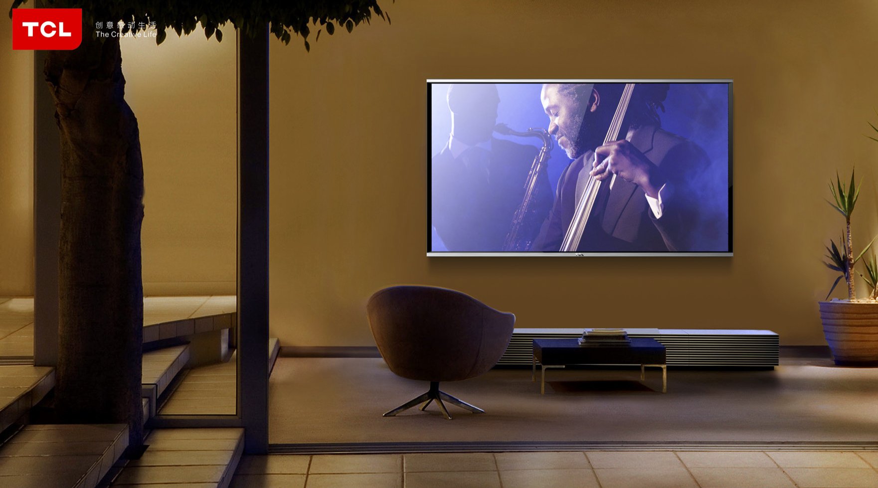 Living room with a large flat-screen TV showing a jazz band performance, a modern chair, a low table with magazines, a potted plant, and warm lighting.
