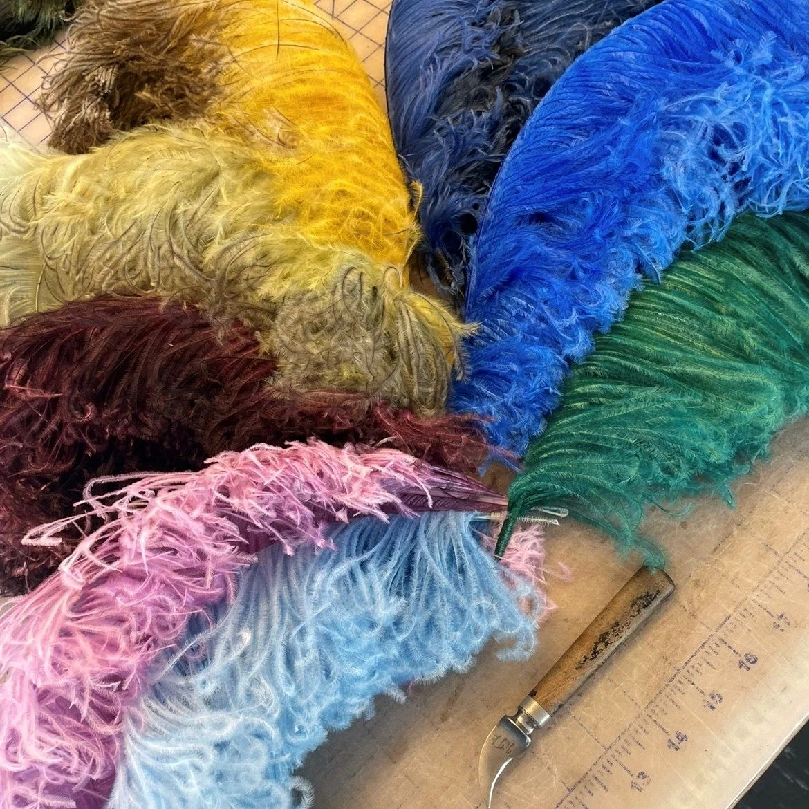 Fjädrar i olika färger som ligger på ett bord bredvid en liten kniv