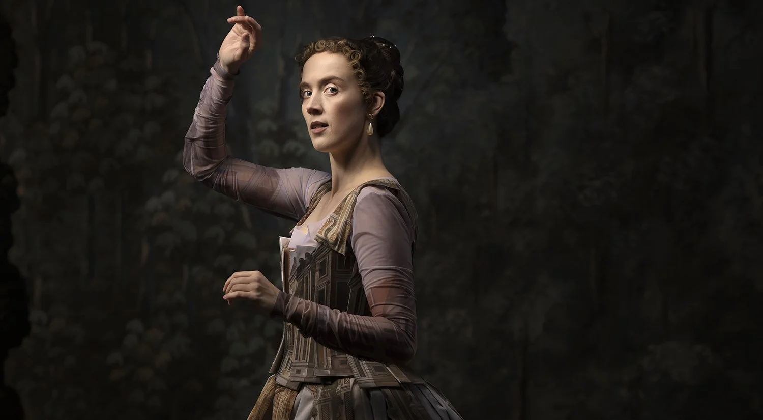 En kvinna i 1800-talskläder står framför en mörk skog.