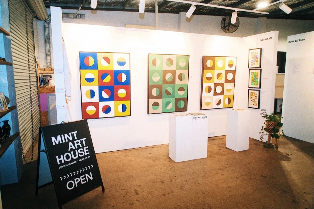 Gallery wall displaying colorful abstract geometric art pieces at Mint Art House, with a black sign indicating 'OPEN'.