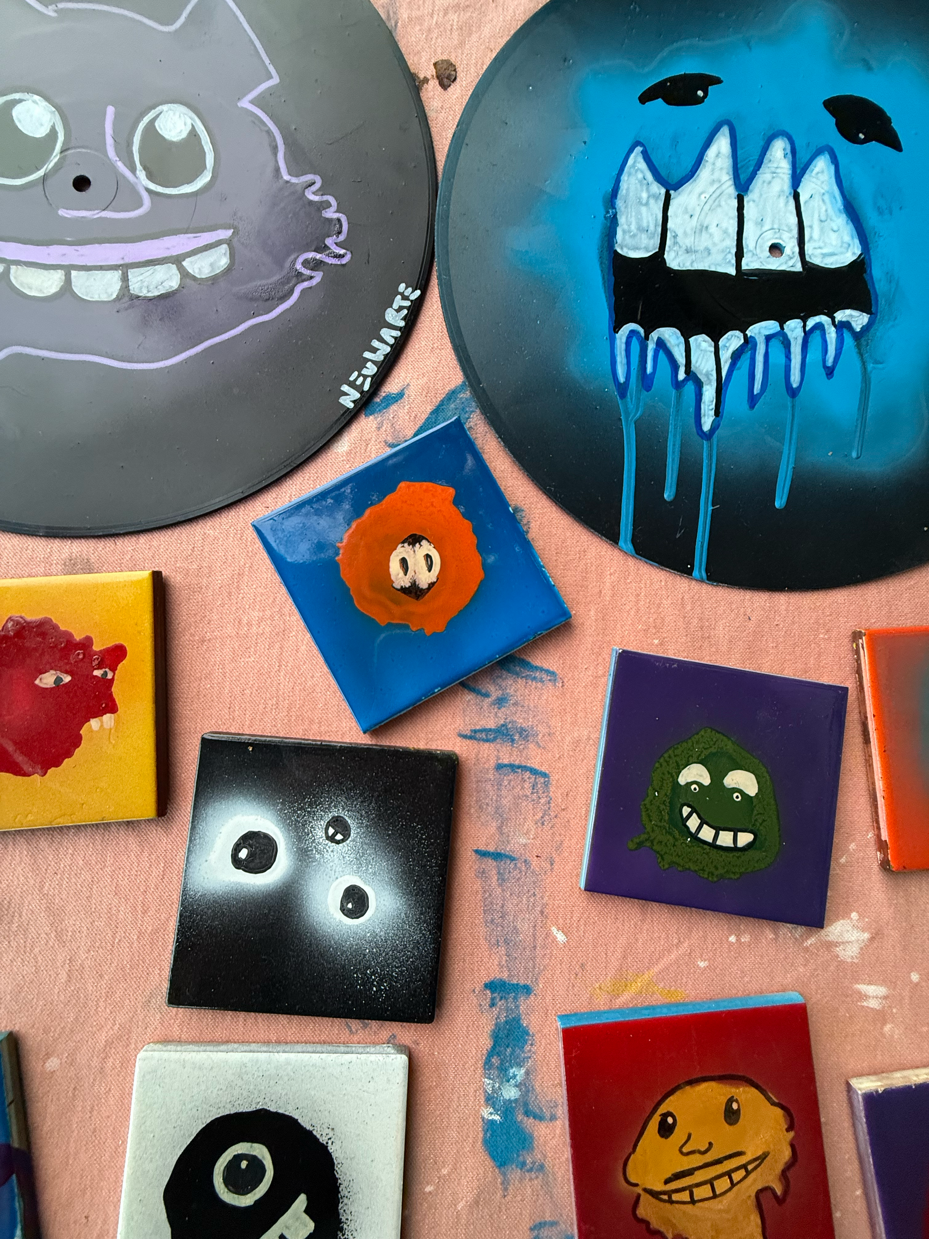 Assorted painted rocks with cartoonish characters and faces, displaying various colors and designs, on a pink fabric surface.