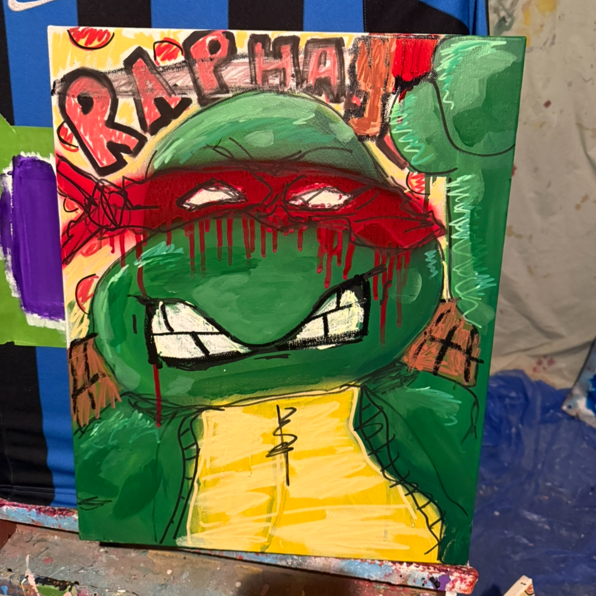 A colorful painting of Raphael from Teenage Mutant Ninja Turtles with a red bandana covering his eyes, showing anger or frustration with blood dripping down his face. The background has the name Raphael in stylised letters.