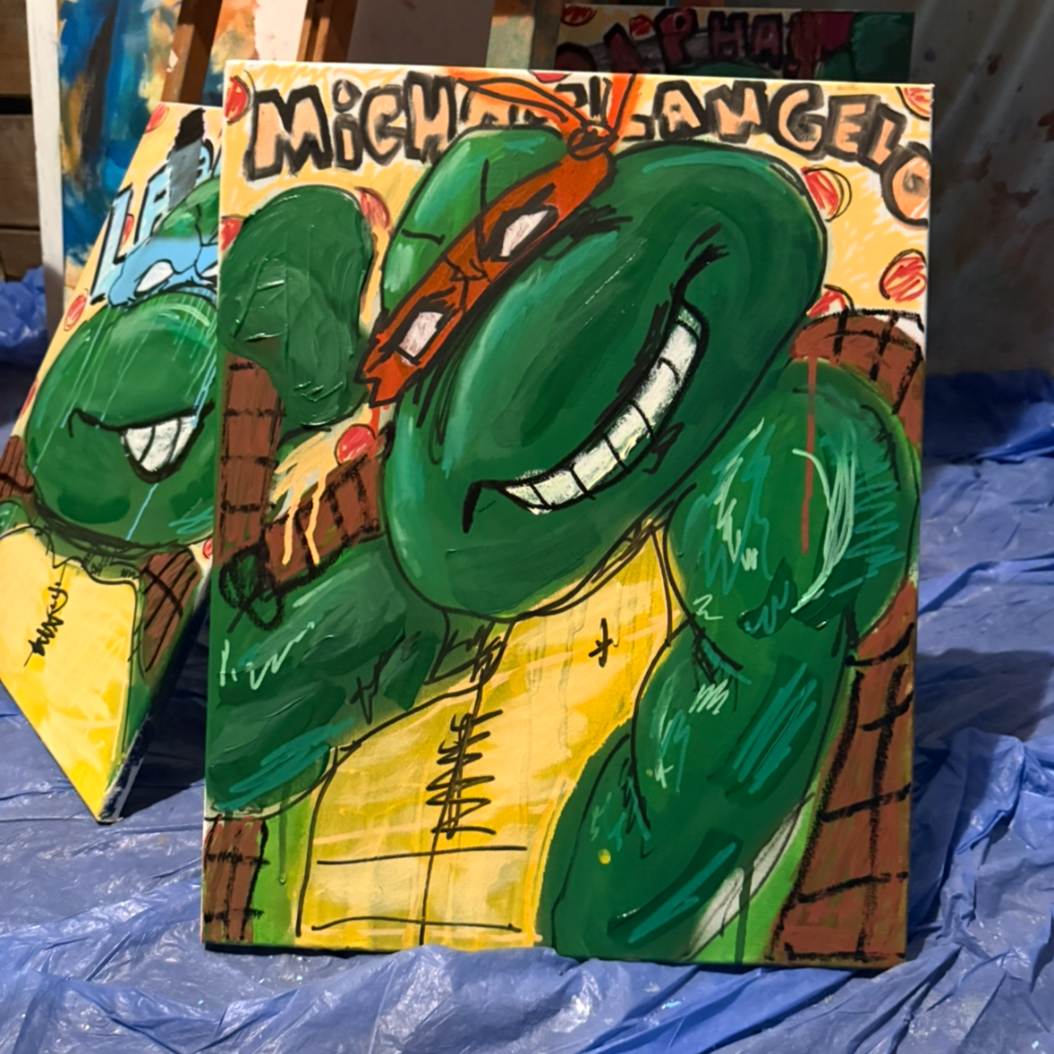 A colorful painting of Michaelangelo, a Teenage Mutant Ninja Turtles character, with a green body, an orange mask, and a big smile, against a yellow background with brown brick details.