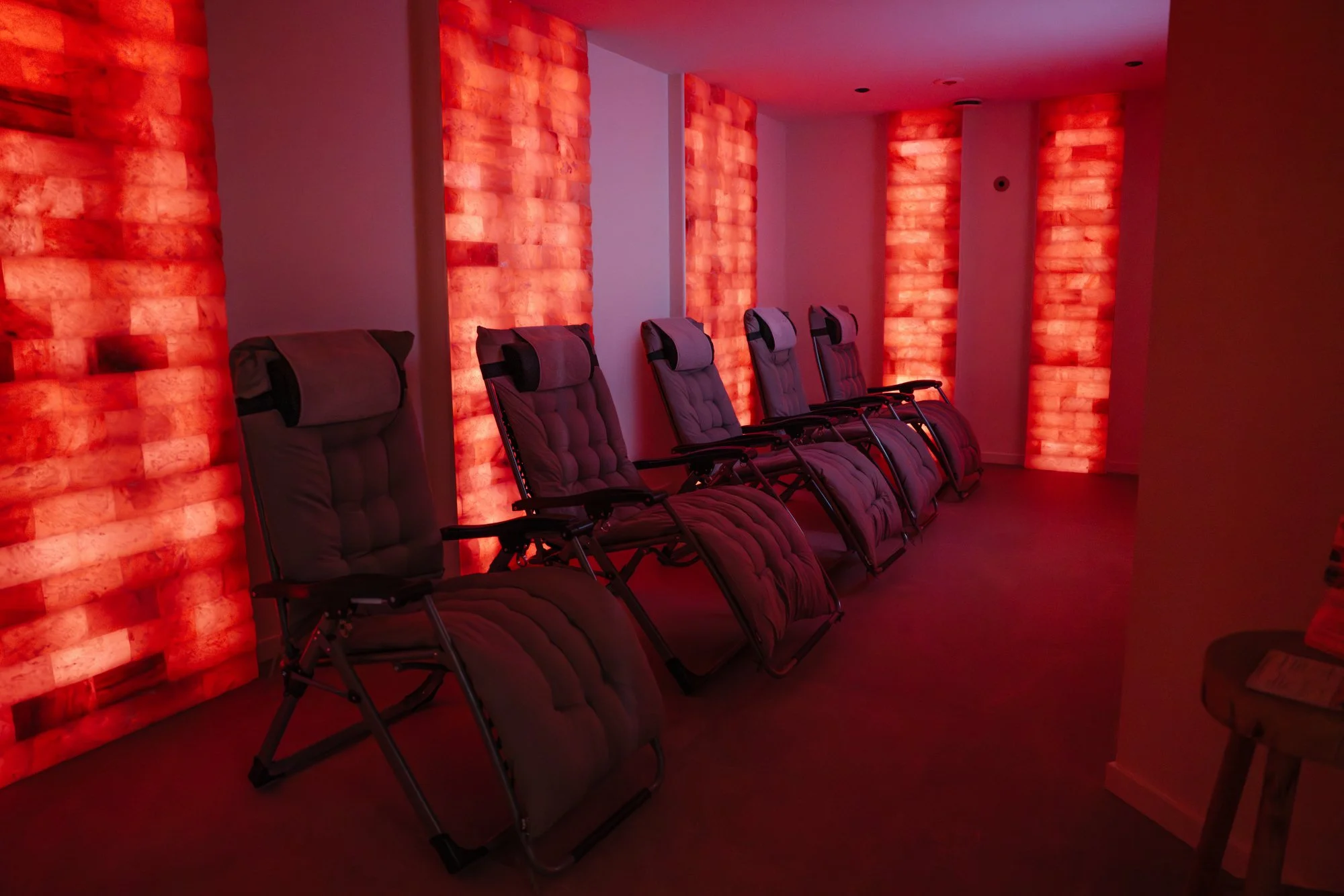 Vijf ligstoelen geplaatst voor een zoutmuur die een rood-oranje gloed uitstralen.