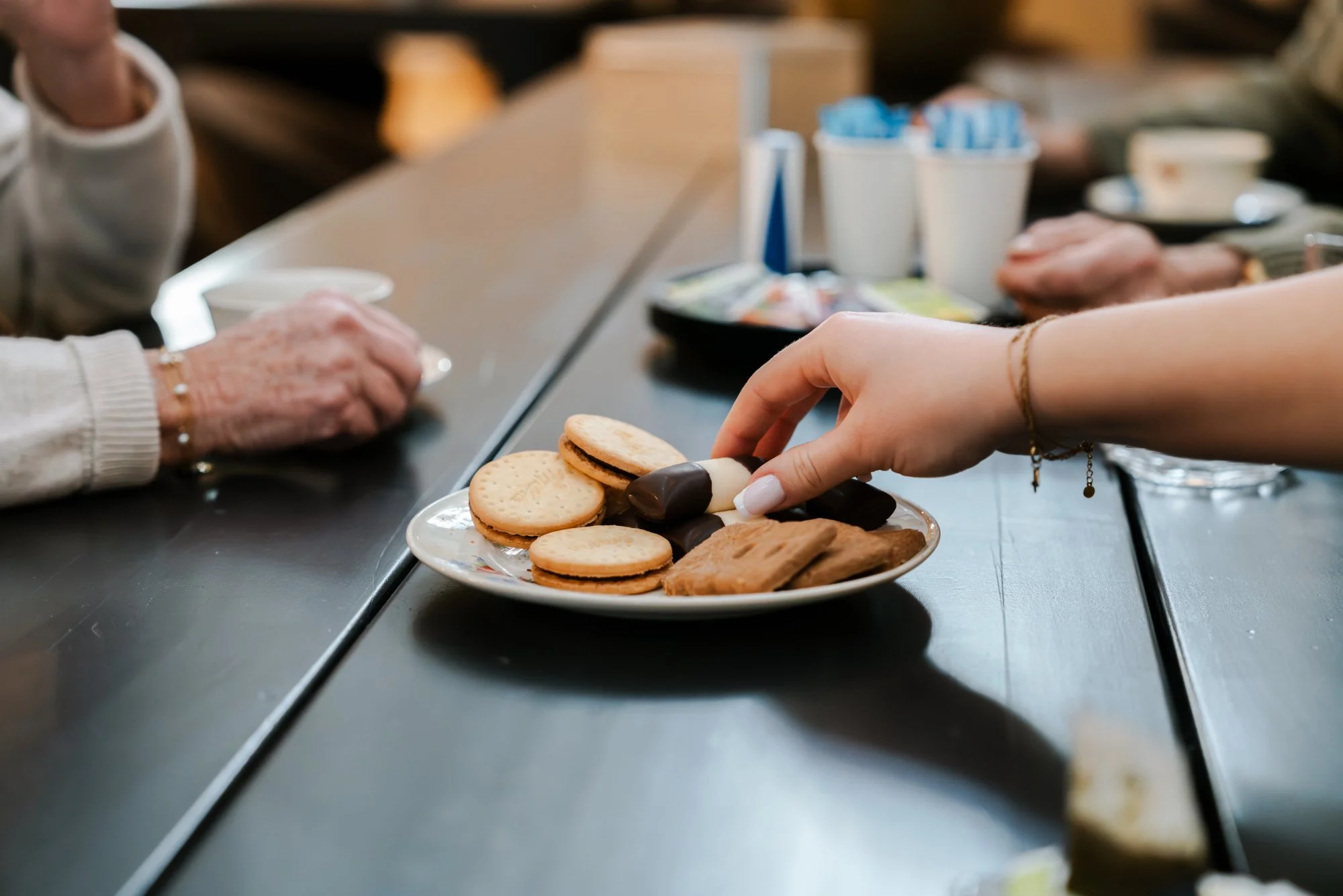Een hand pakt een schotel met koekjes, chocolade en koekrepen over een donkere tafel