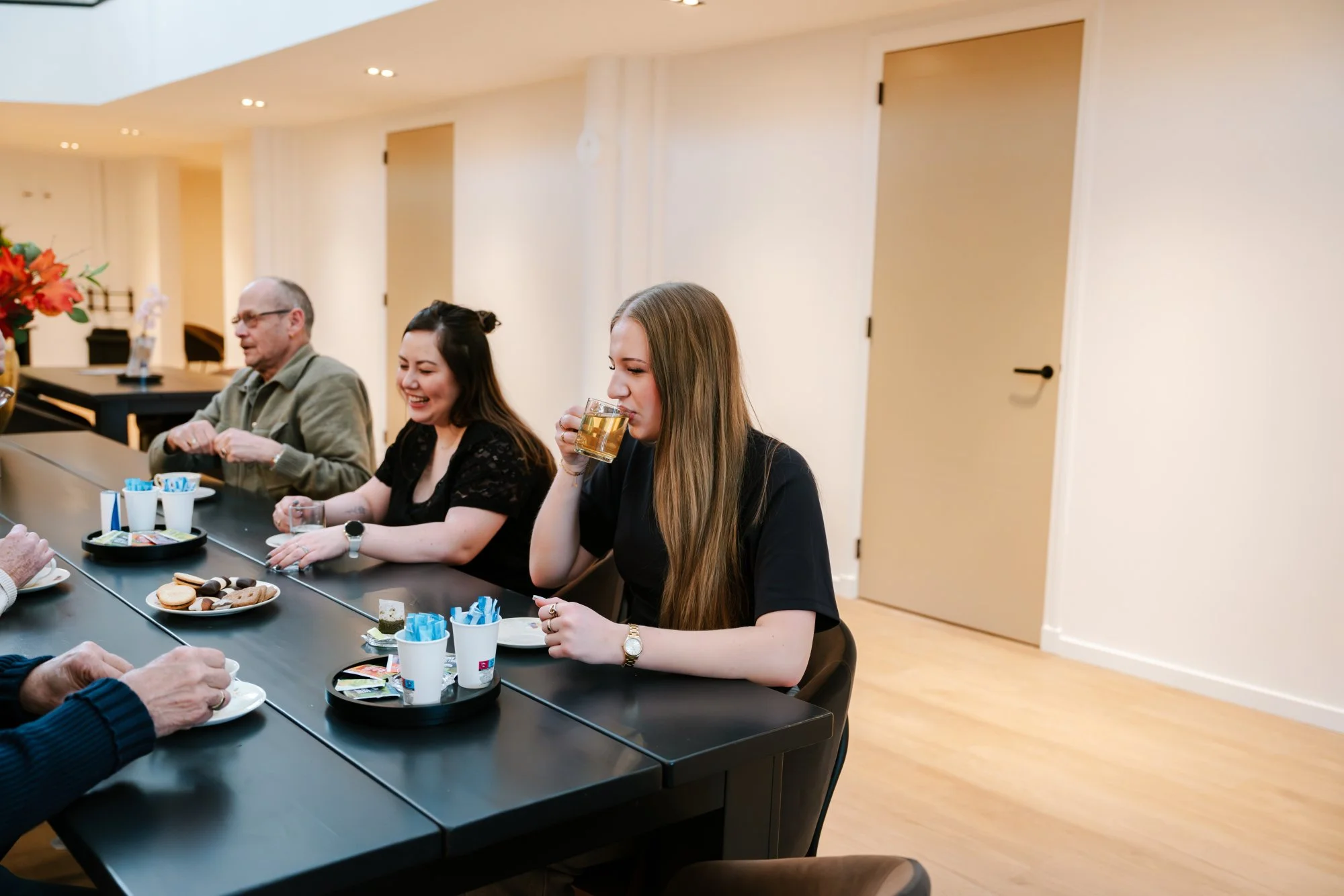 Mensen zitten aan een tafel met koffie, cake en snacks in een verbouwde kerk met lichte muren 
