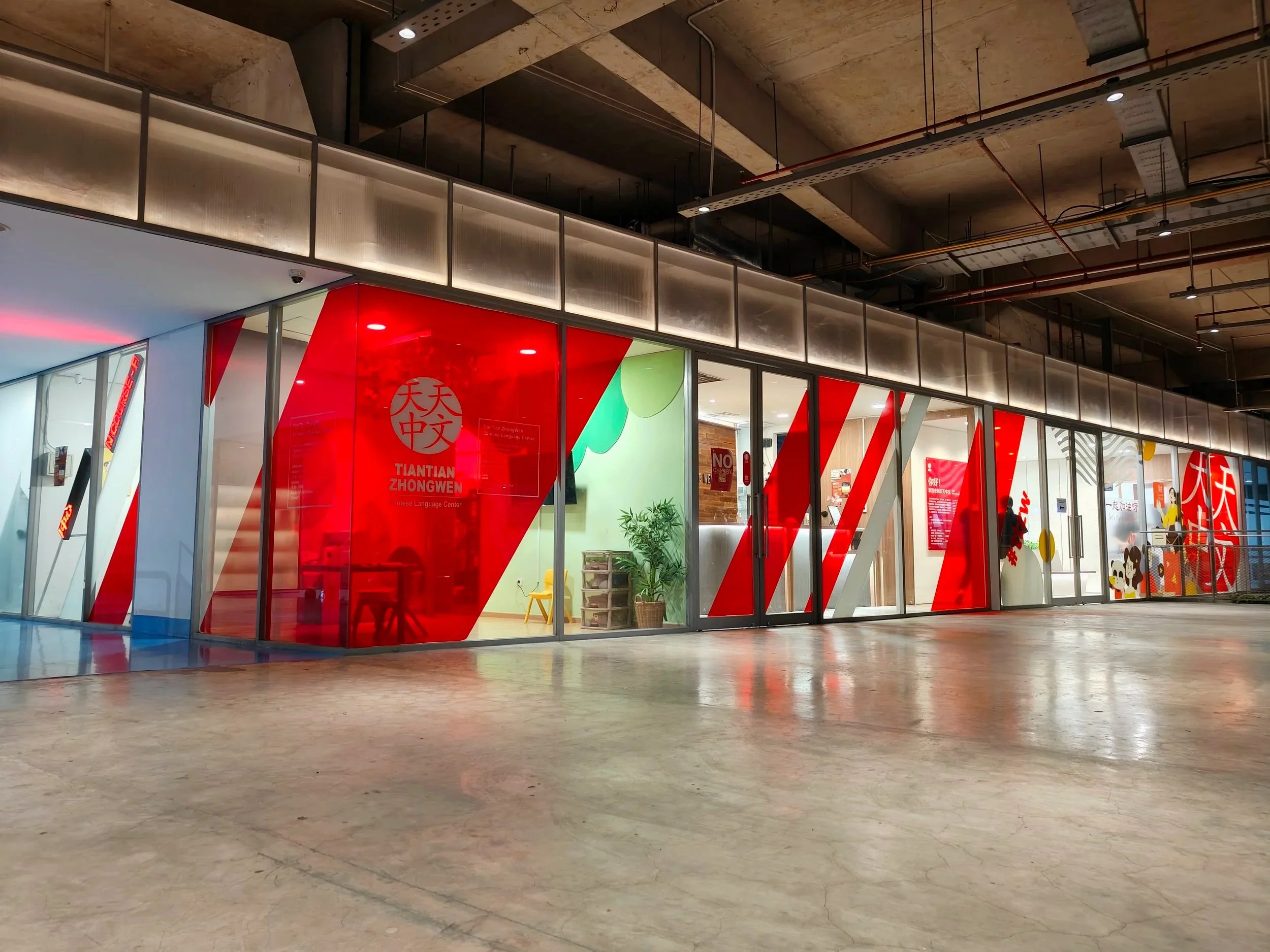 Exterior view of Tiantian Zhongwen's Spaizio Tower branch with glass walls and red diagonally striped panels.