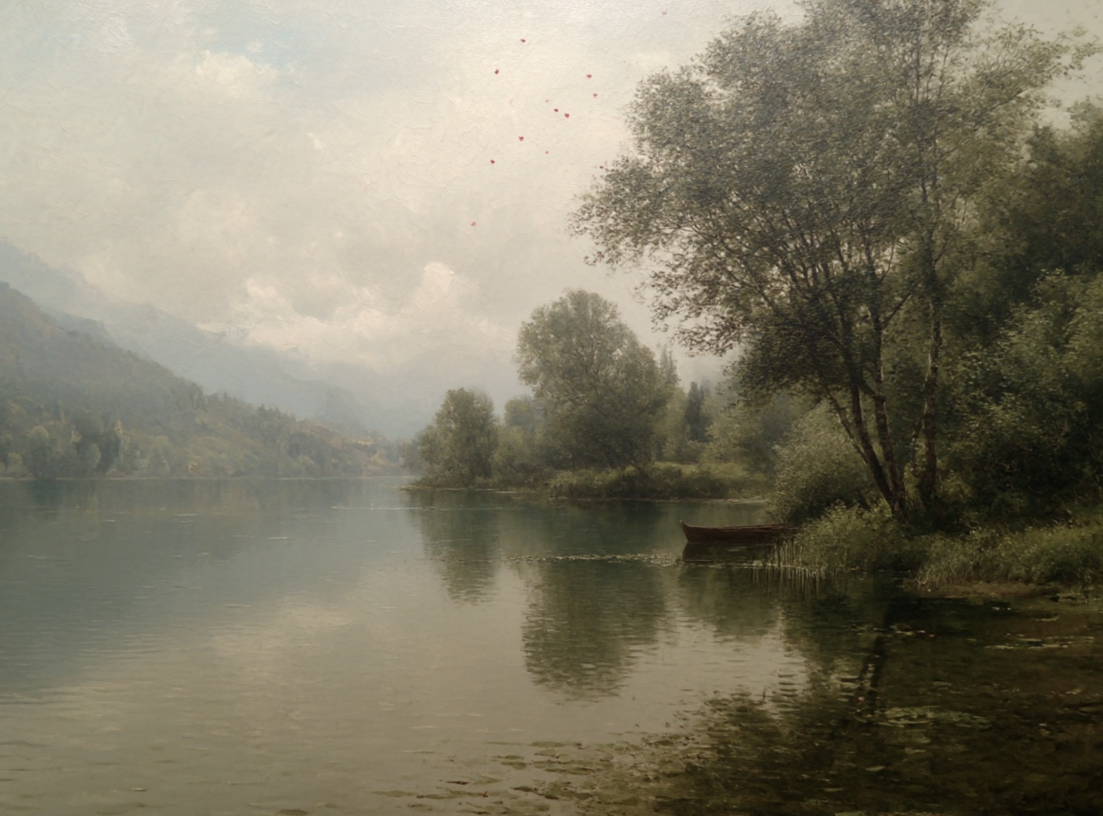 A calm river with reflections of tall trees on the shoreline, surrounded by distant mountains under a cloudy sky.