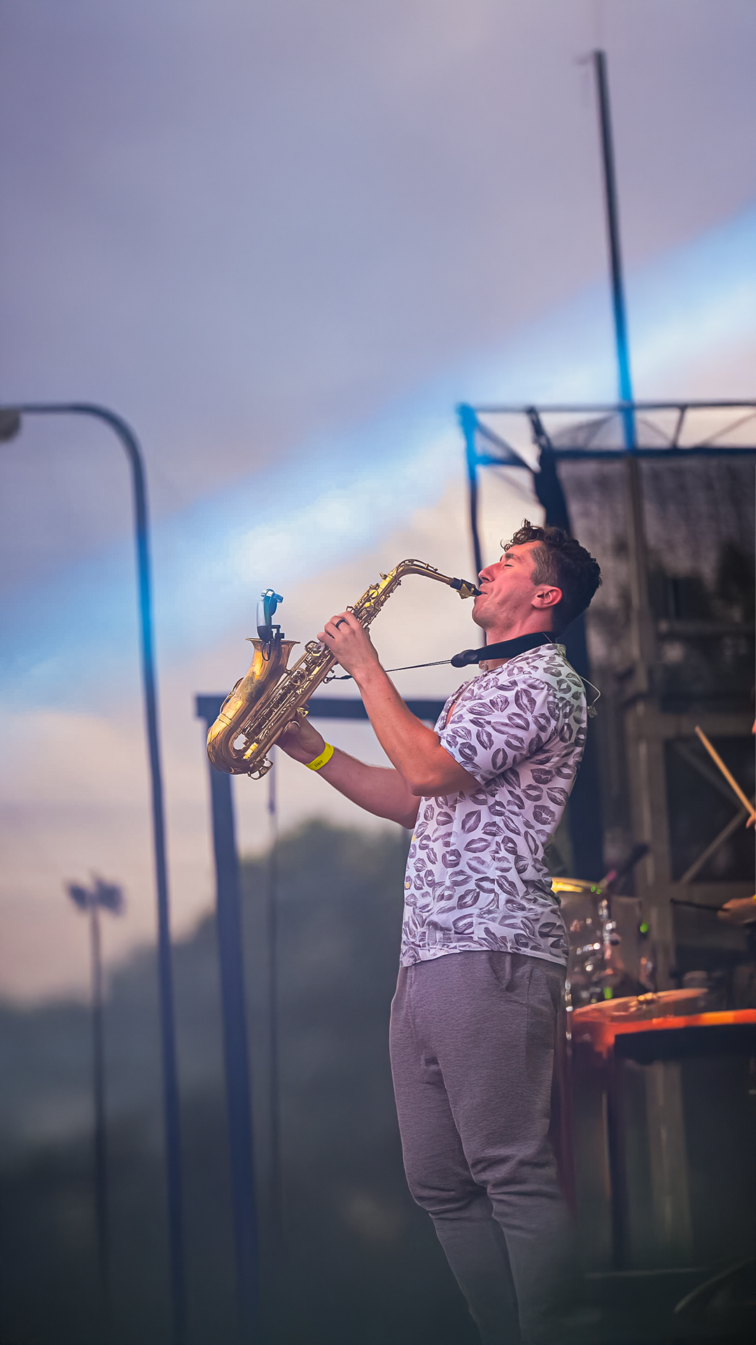 A man playing a saxophone on stage at an outdoor concert during sunset.