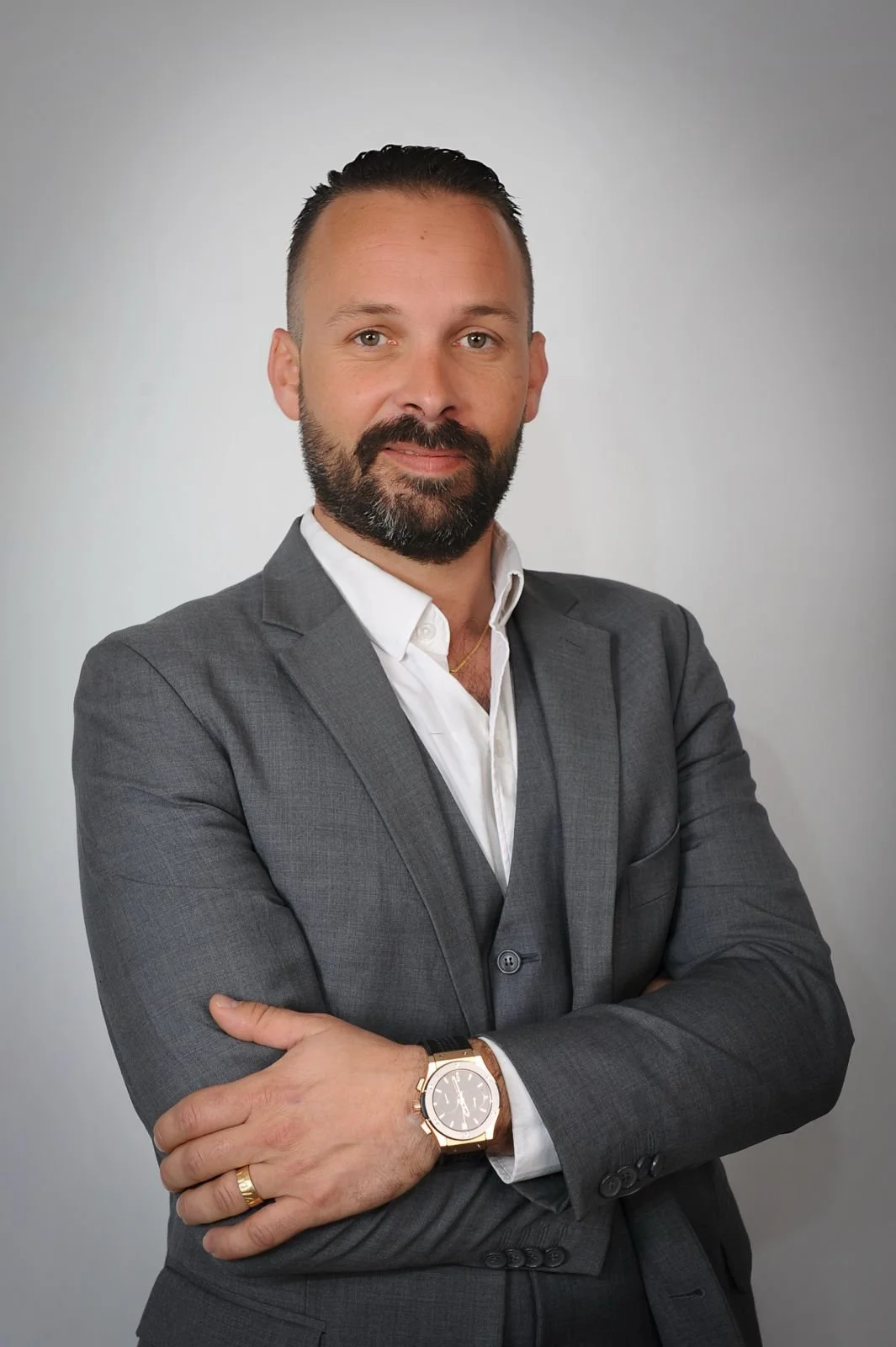 Portrait d'un homme d'affaires en costume gris, portant une montre en or et un anneau à la main gauche, se tenant dans un fond gris