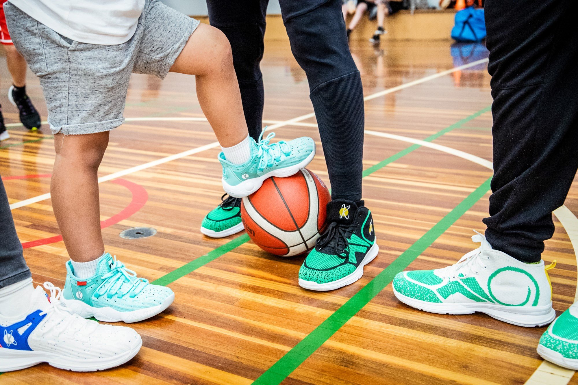Kids and adults playing basketball in a gym, with one child stepping on a basketball as they prepare to jump.
