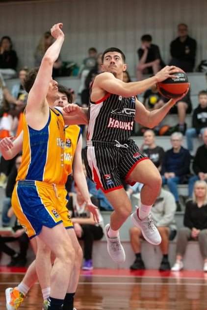 Basketball player in black jersey jumping for a shot while an opponent in yellow jersey attempts to block