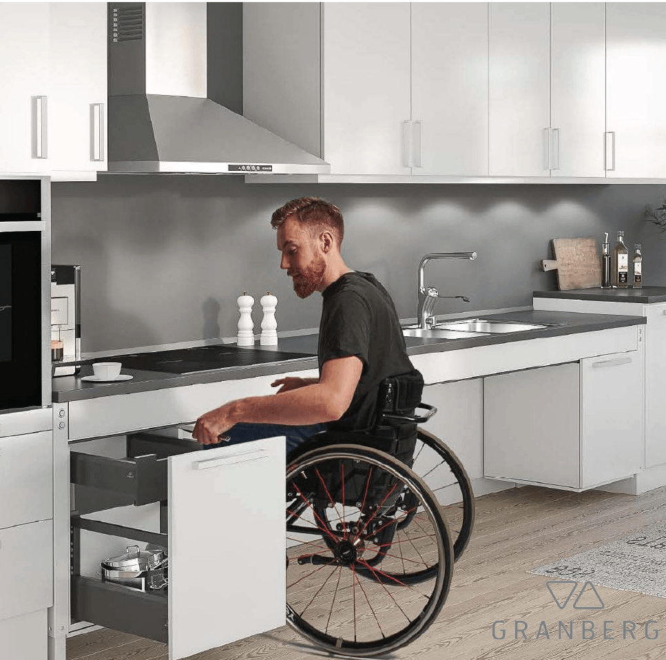 Disabled man in wheelchair using an accessible kitchen using a pull out drawers and height adjustable kitchen counter on lift.