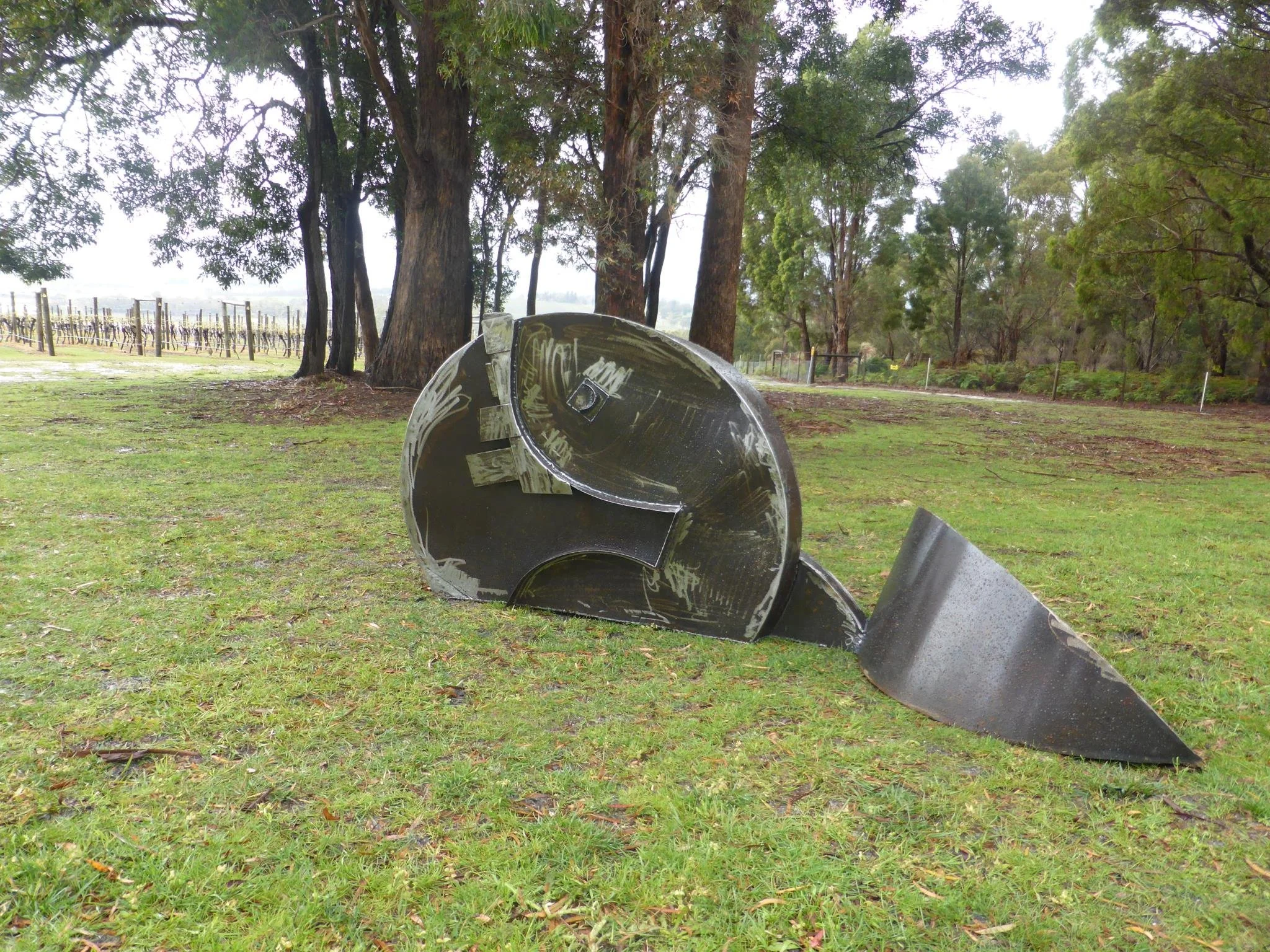 A Neil Grose sculpture on grass in a park with tall trees in the background.