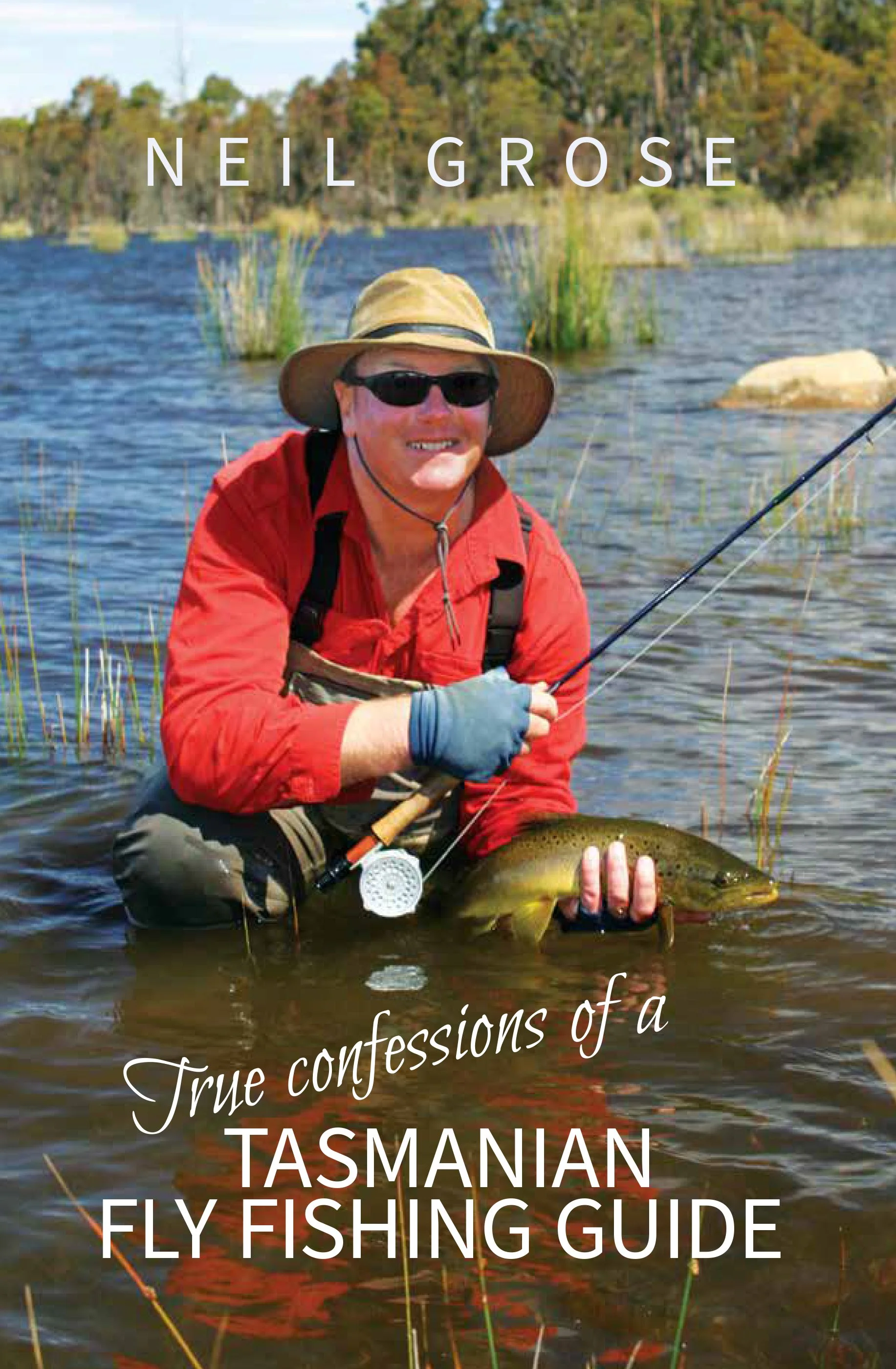 A man with sunglasses and a wide-brimmed hat holding a fishing rod and a large fish in a lake with trees in the background. Overlaid text reads, 'True confessions of a Tasmanian fly fishing guide'.