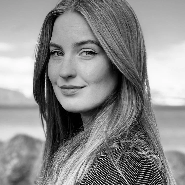 A black and white photo of Rannveig Jónsdóttir, outdoors with a blurred landscape background.