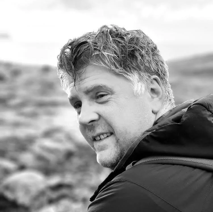 A black and white photo of Ingi Björn Guðnason, smiling, outdoors, wearing a dark jacket.