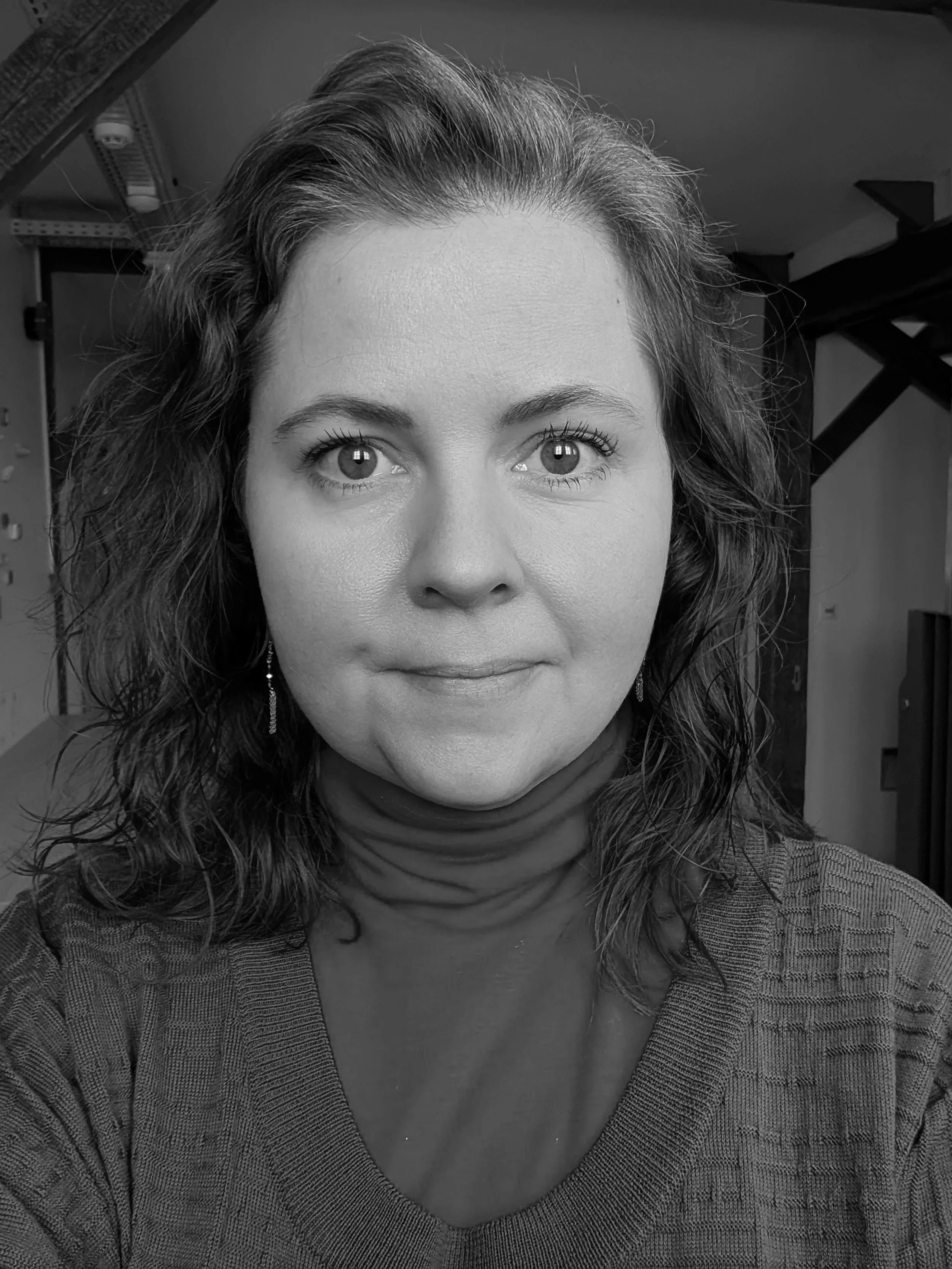 A black and white photo of Tinna Ólafsdóttir, wearing earrings and a turtleneck, looking directly at the camera.