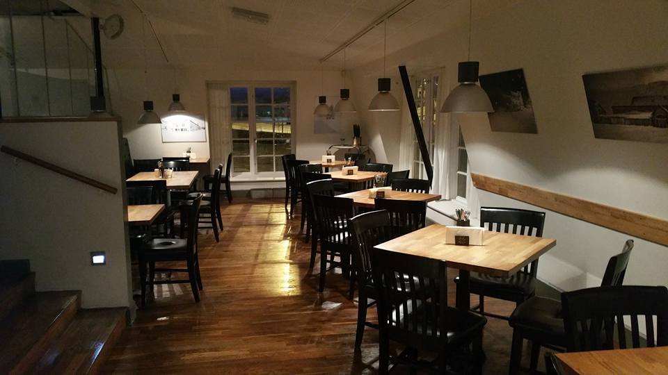 Edinborg Bistró restaurant with wooden floors, black chairs, wooden tables, pendant lights, and framed photographs on the white walls.