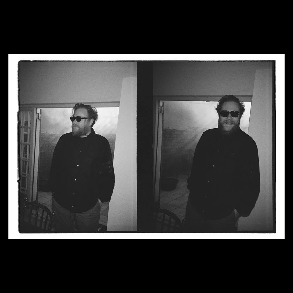 Black and white photograph of a man in sunglasses posing in front of a landscape background, displayed as a mirrored image with two identical images side by side.