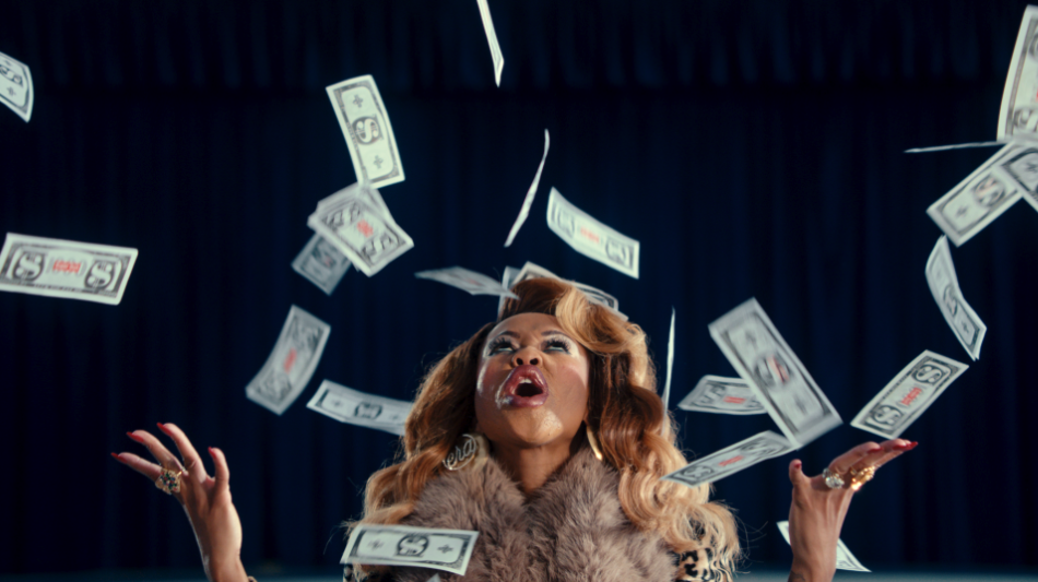 Woman with blonde hair, fur coat, and jewelry throws money into the air in front of a dark curtain.